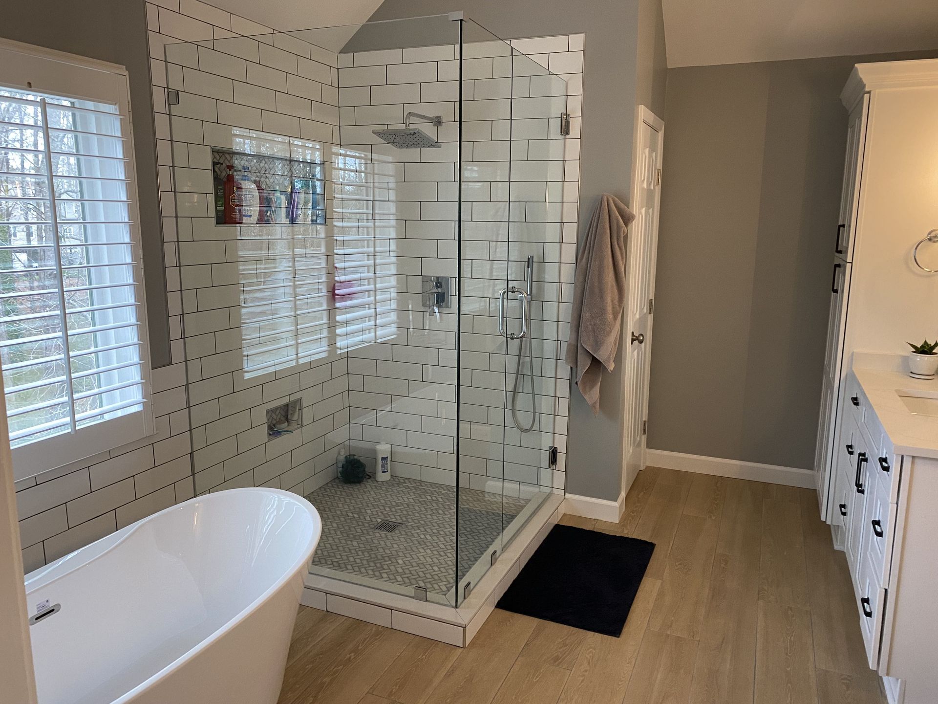 Modern bathroom with glass shower, white tub, and light wood floors.