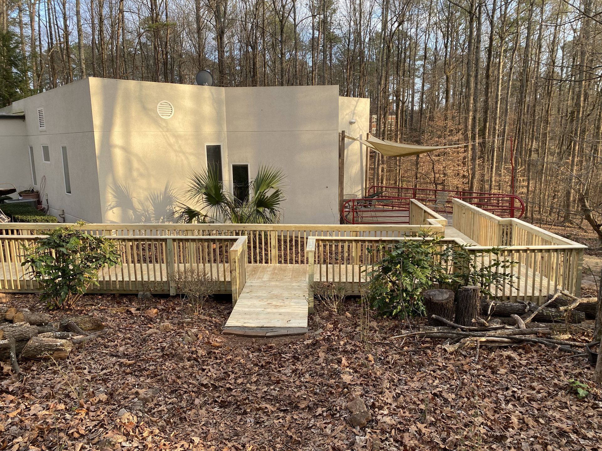 Wooden deck with railing leading to a light-colored building in a wooded area.