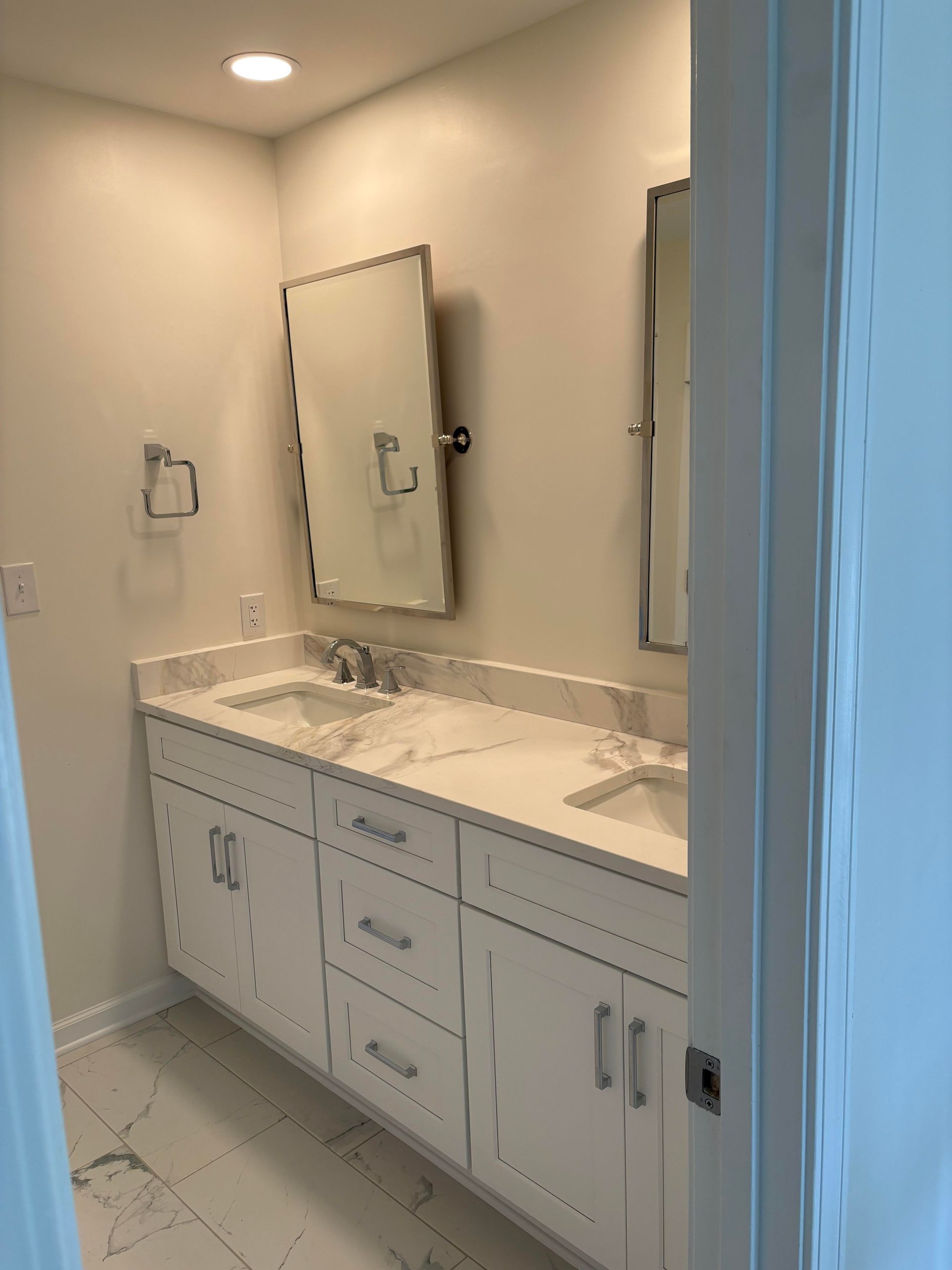 White bathroom with double vanity, marble countertop, and rectangular mirrors.
