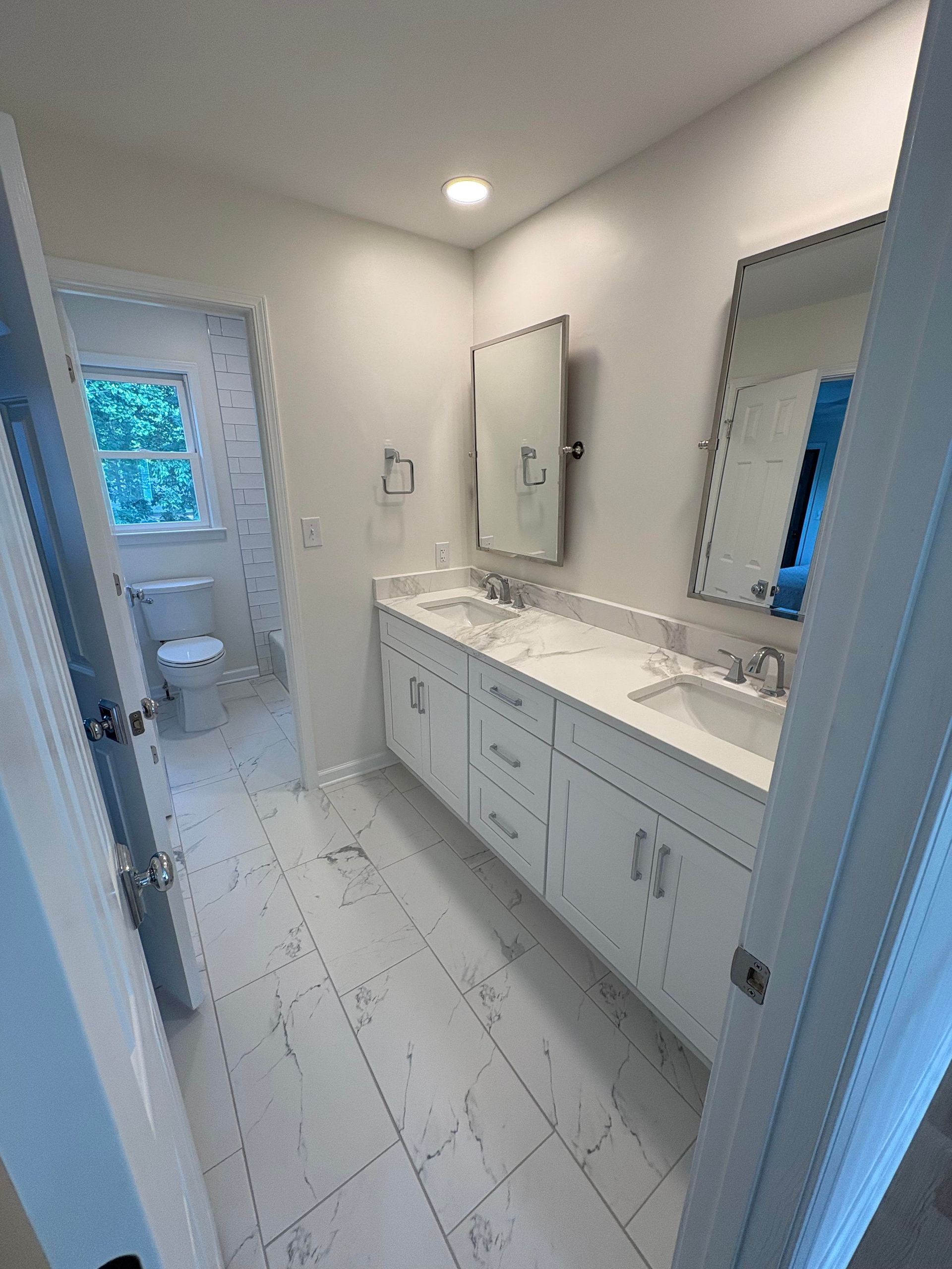 Bright, renovated bathroom with white cabinets, marble-look floor, and dual sinks.