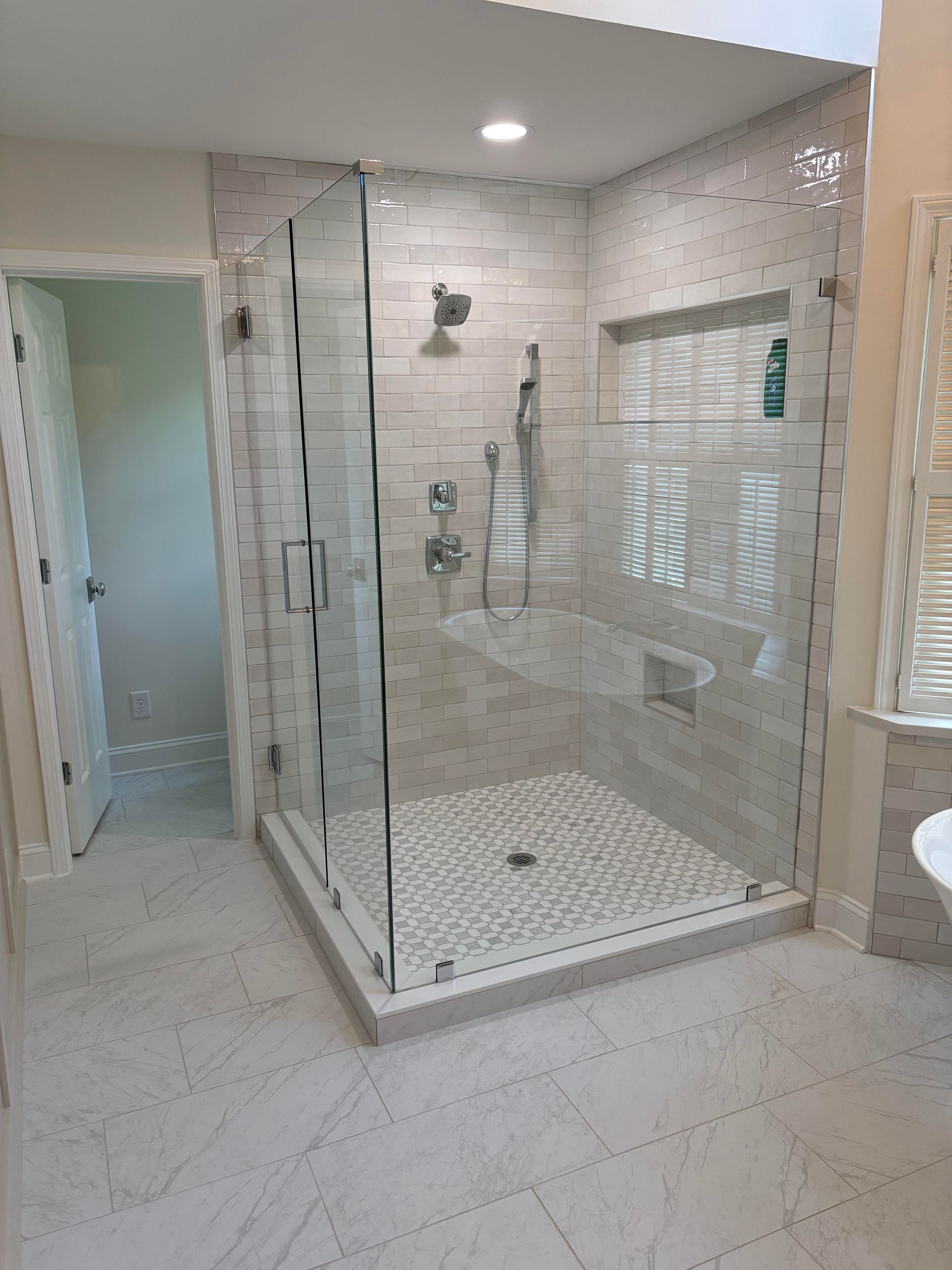 Modern shower with clear glass doors and white tile walls and floor.