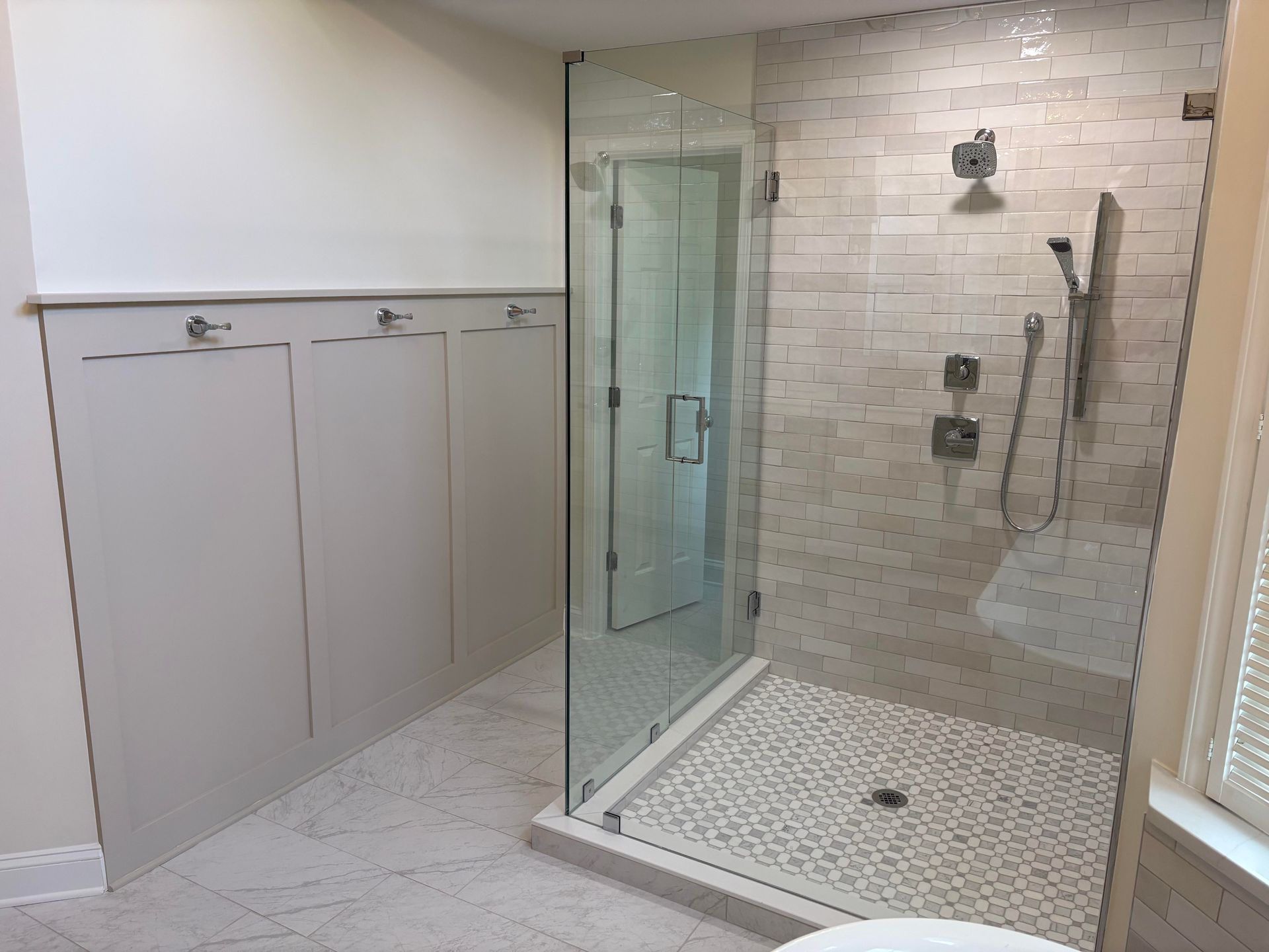 Modern bathroom with glass shower, pebble floor, and white tiled walls.