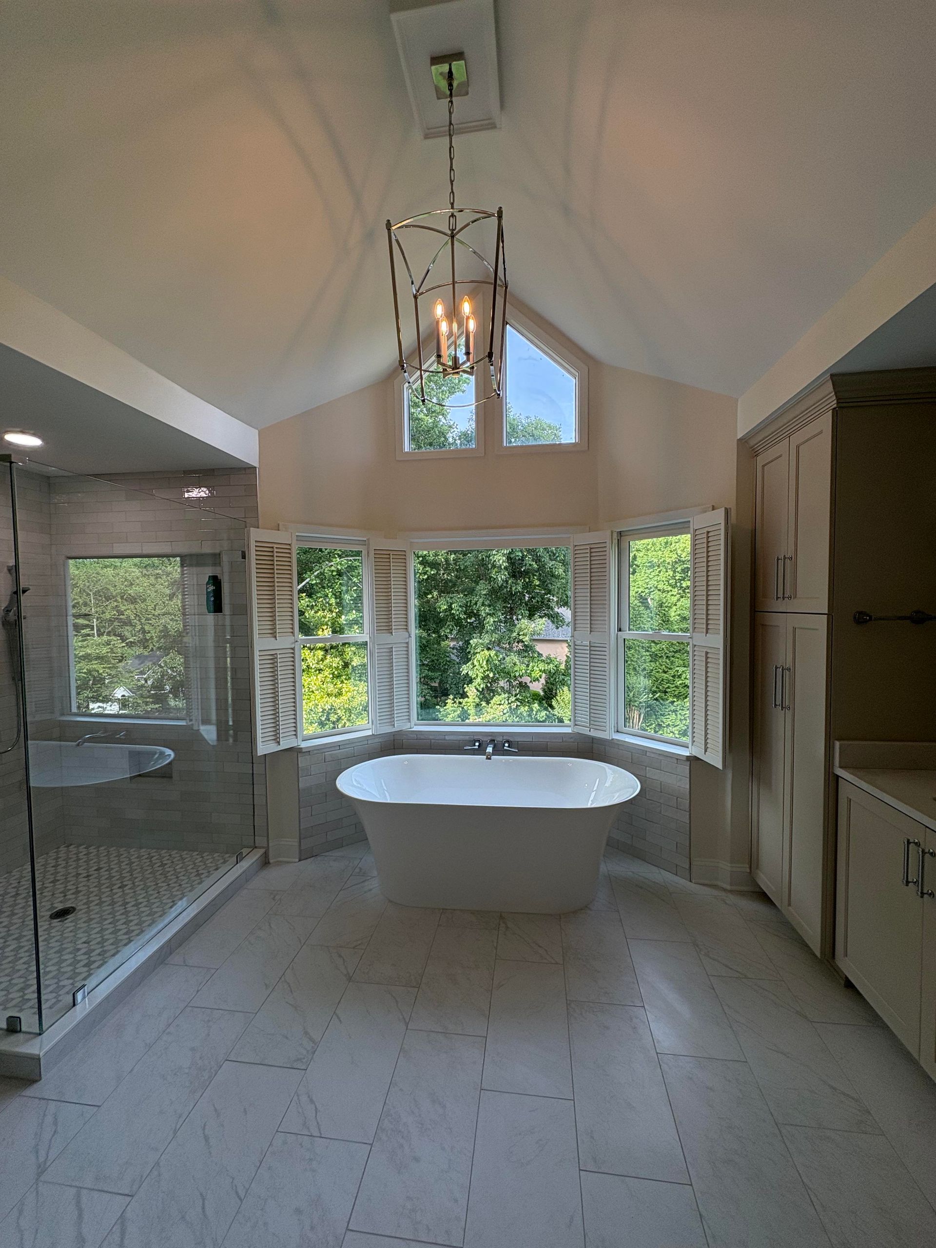Luxurious bathroom with a freestanding tub in front of a bay window and a chandelier.