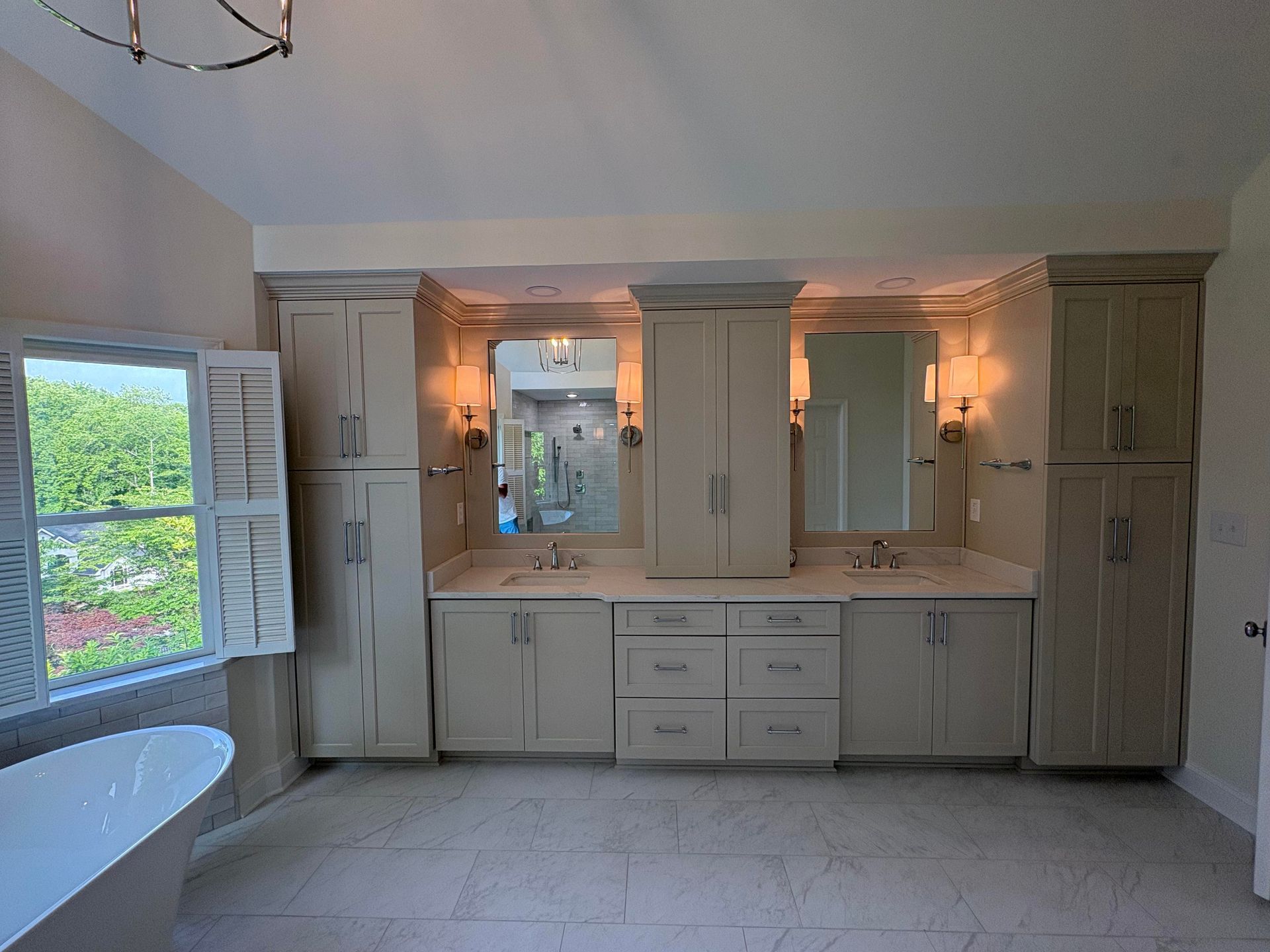 Bathroom with double vanity, two mirrors, and tall storage cabinets in light gray. Window with shutters.
