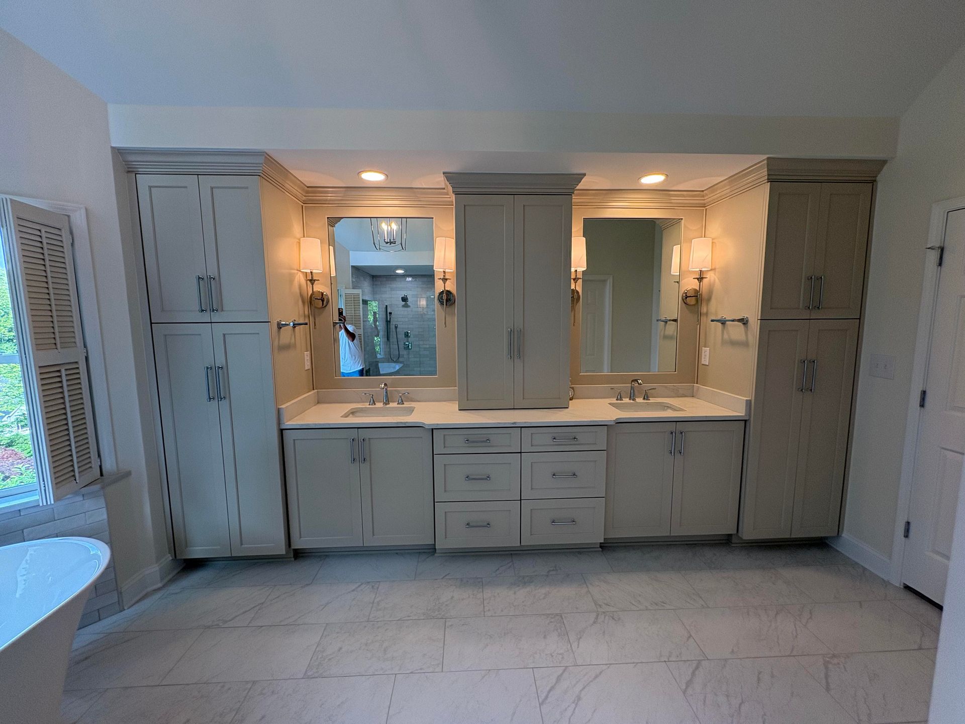 Bathroom with two vanities, mirrors, and tall cabinets in neutral tones.
