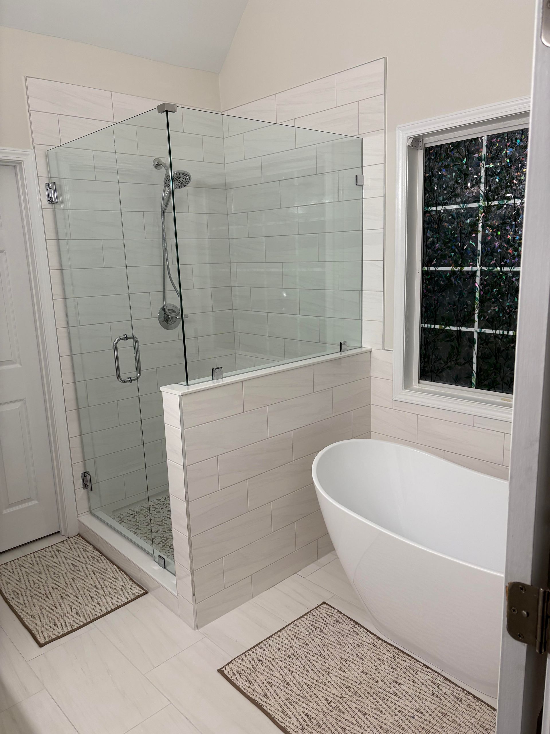 Modern bathroom with glass shower, freestanding tub, and white and gray tiling.