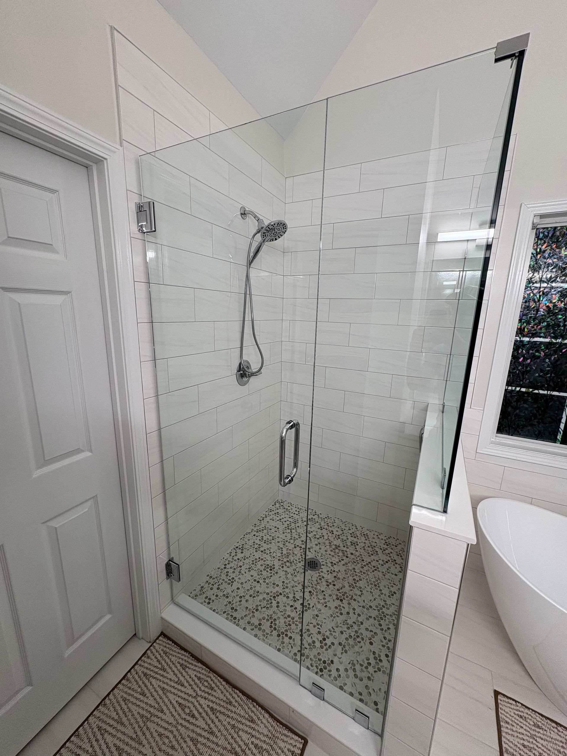 Glass shower with white and grey tile, silver hardware, and a pebble floor.