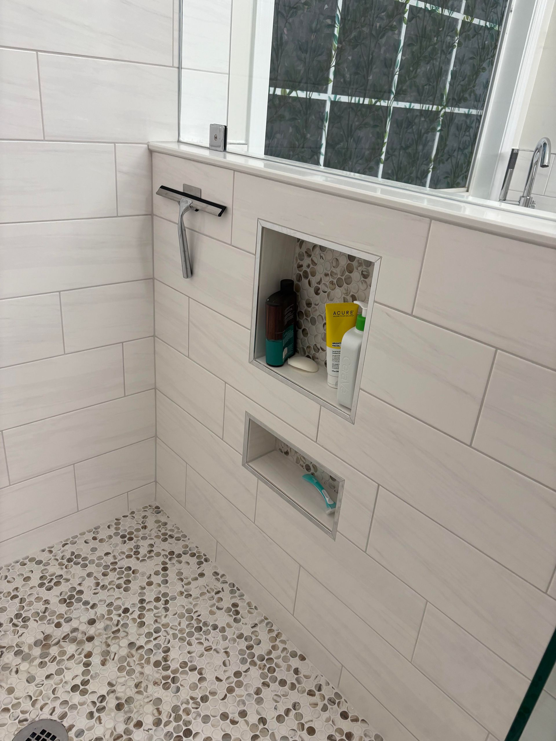 White tiled shower with pebble floor, built-in shampoo niches, and glass shower door.