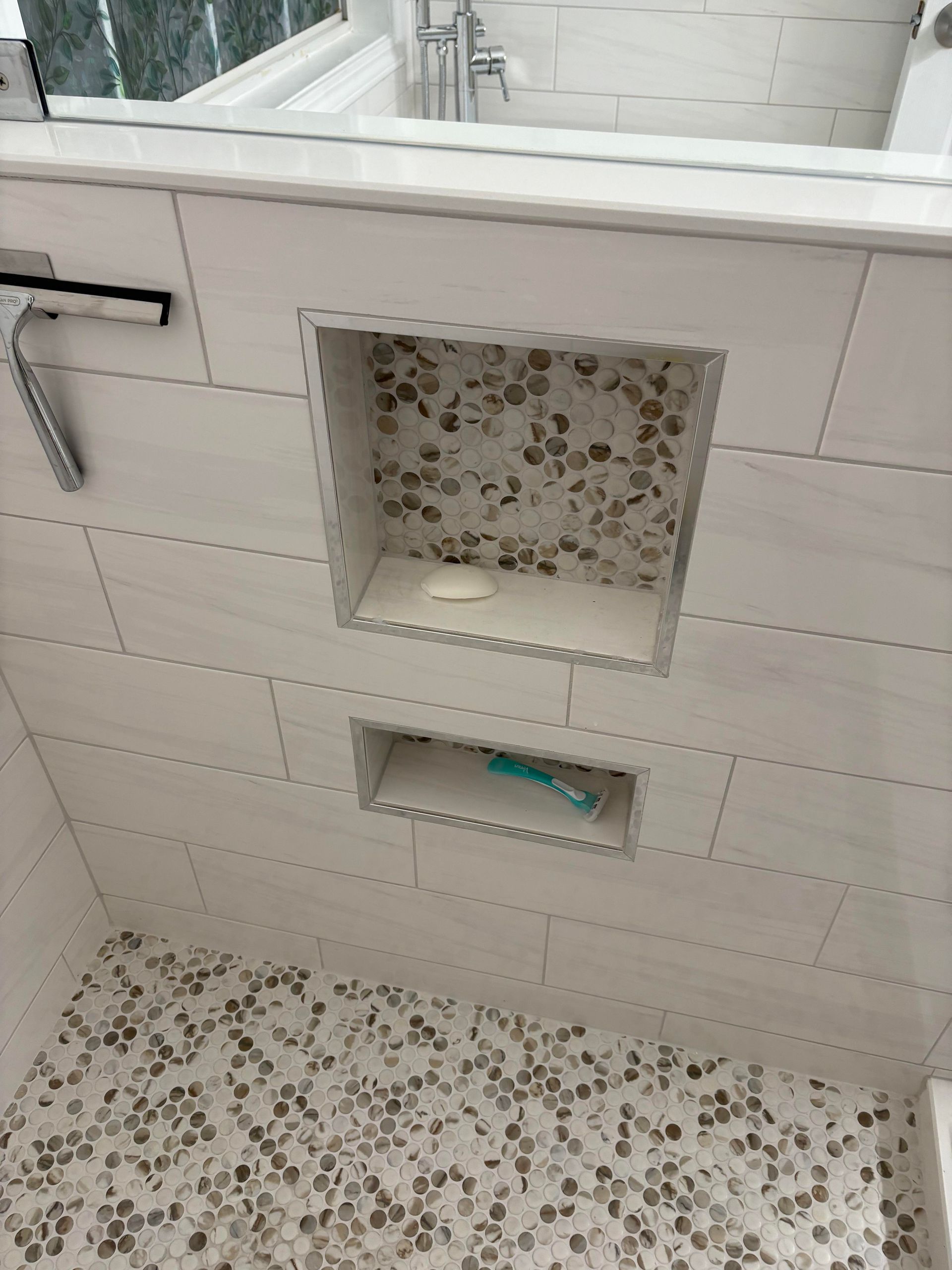Shower with tiled walls and pebble stone floor, with built-in storage shelves.
