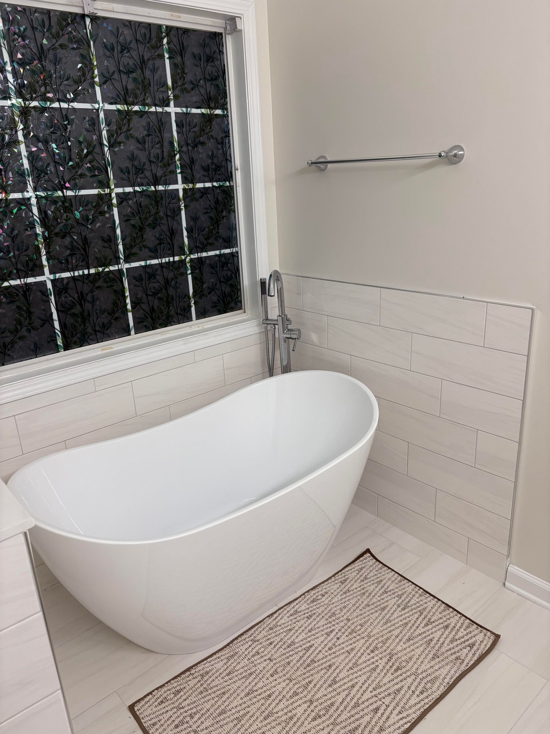 White freestanding bathtub in a bathroom with window, tile, and a rug.