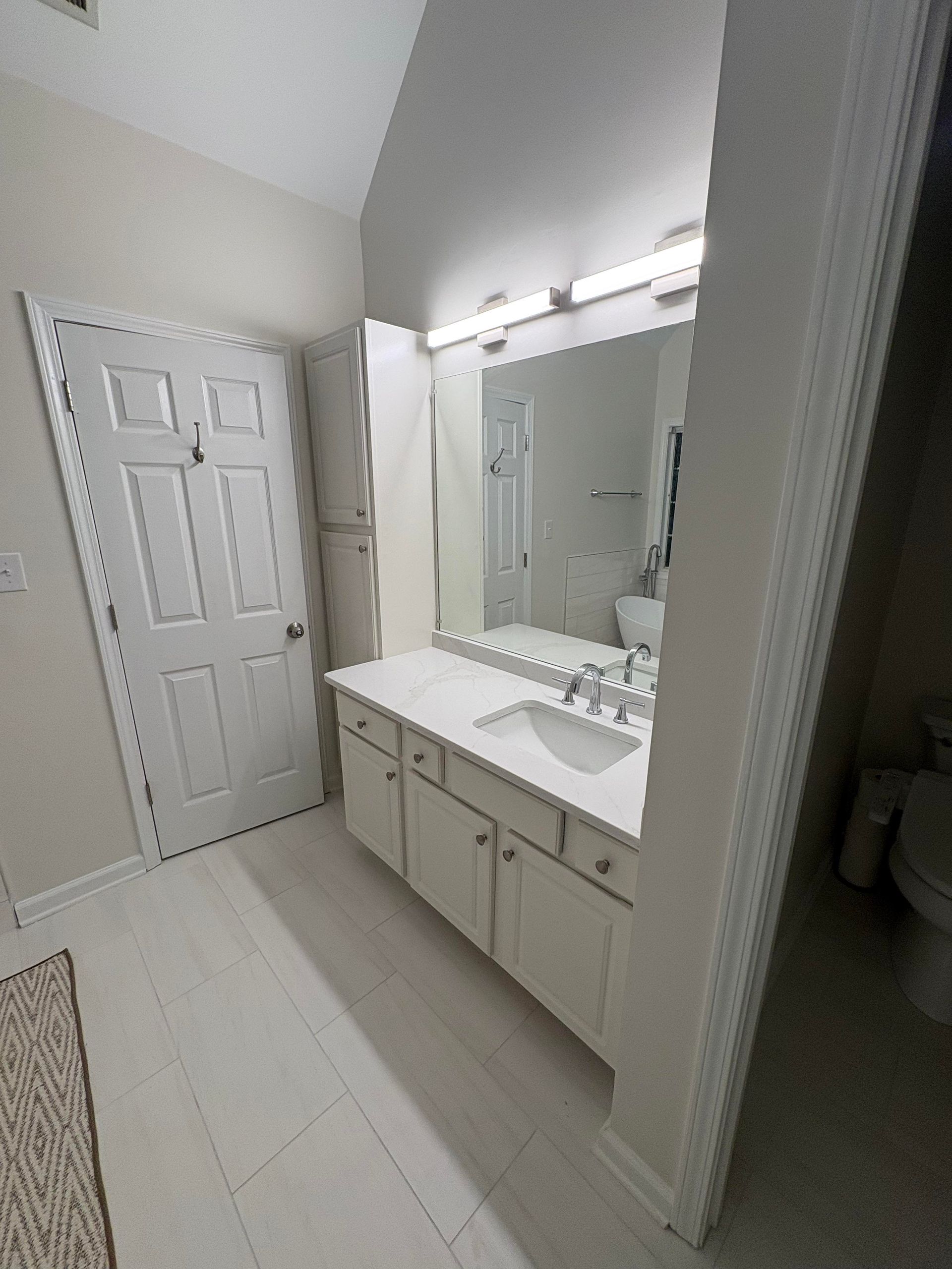 Bathroom with white cabinets, countertop, and door. Mirror reflects the toilet.