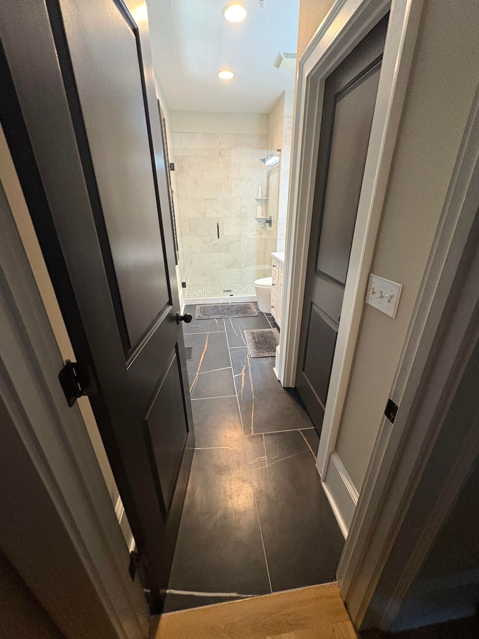 Narrow hallway with dark doors, leading to a bathroom.