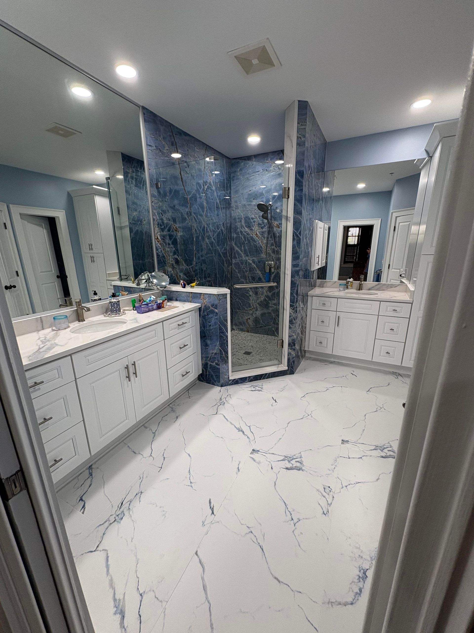 Spacious bathroom with blue accent wall, double sinks, and marble-like flooring.