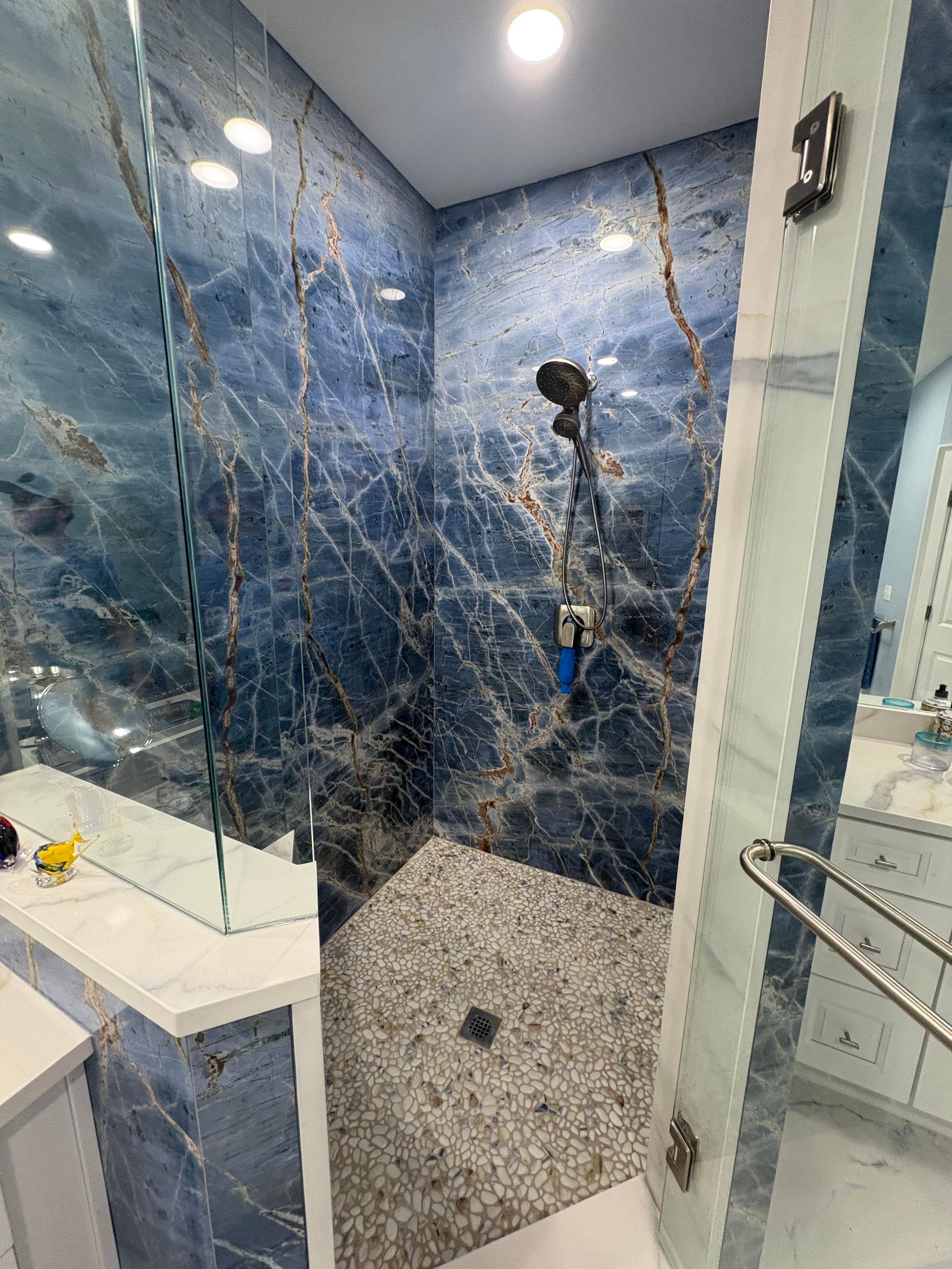 Blue marble-tiled shower with pebble floor, glass door, and silver fixtures.