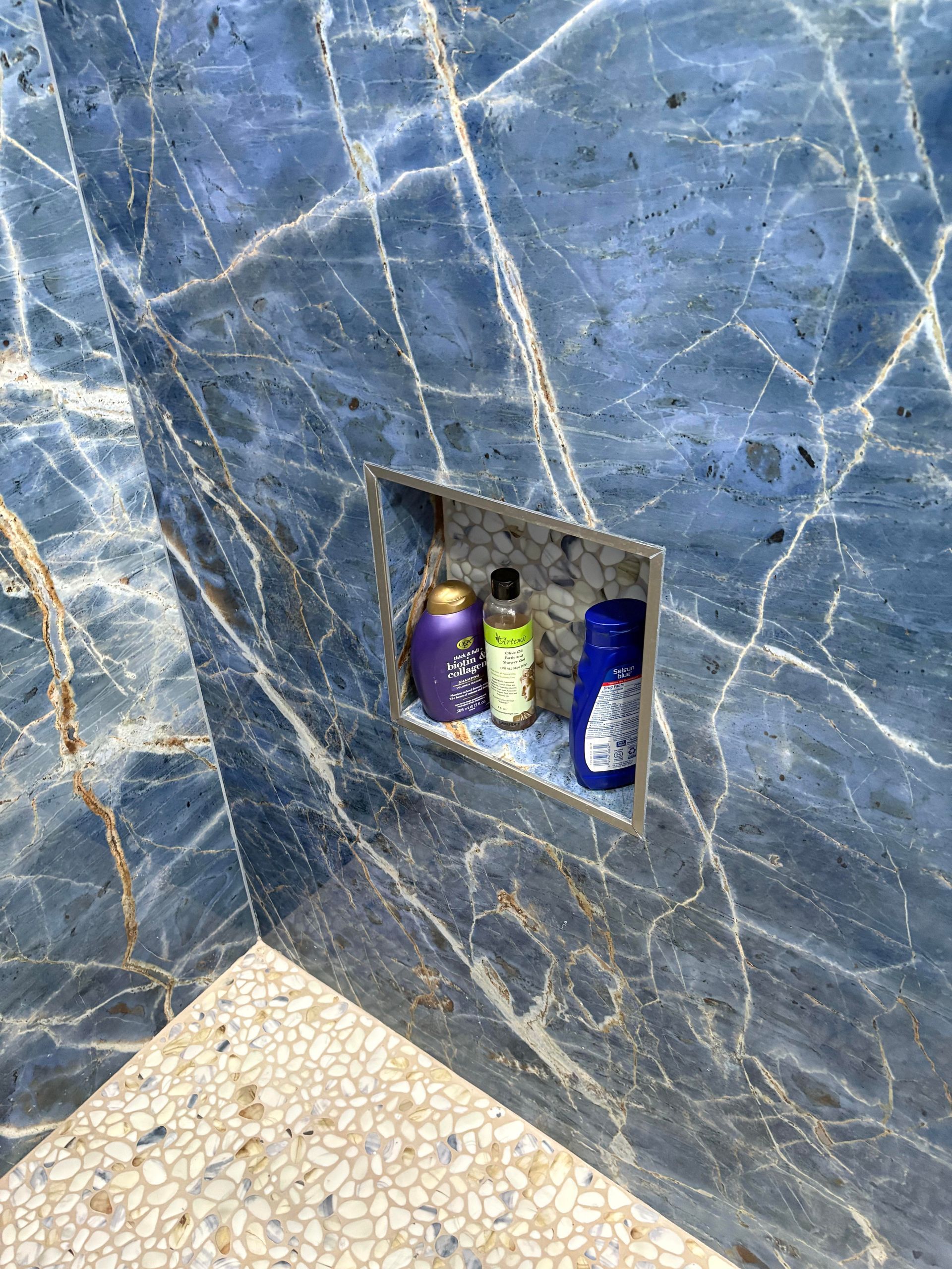 Blue marble shower with built-in shelf holding three bottles of toiletries.