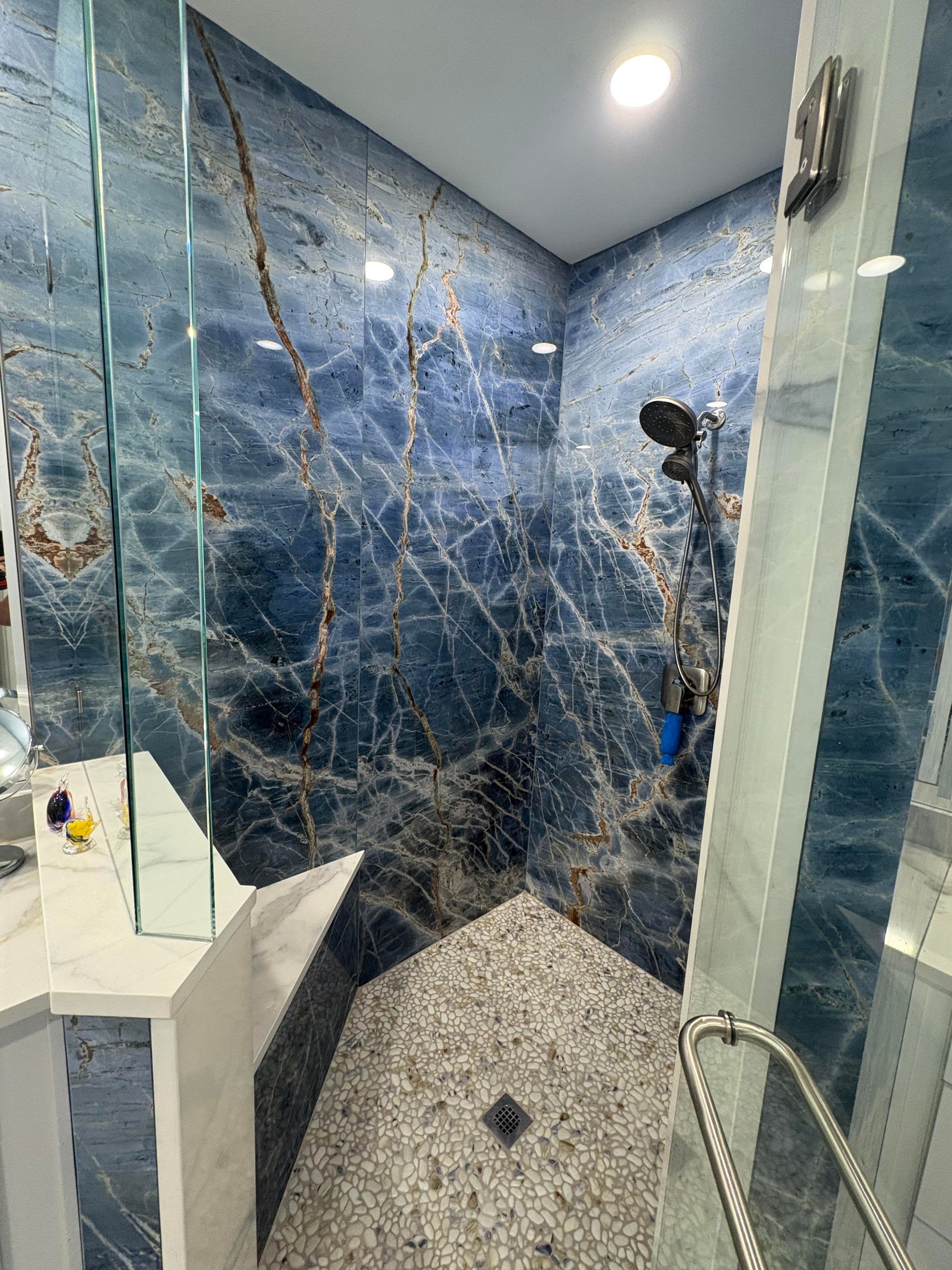 Blue marble-tiled shower with a pebble floor, glass doors, and chrome fixtures.