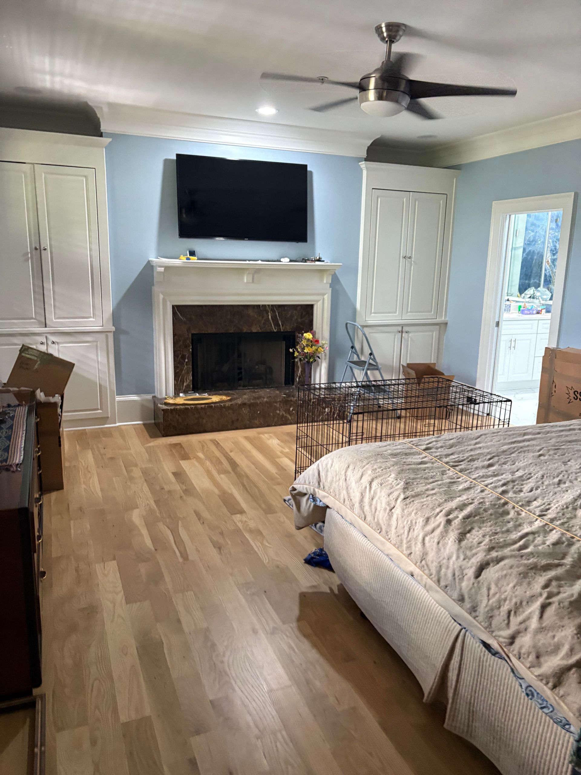 Bedroom with fireplace, built-in cabinets, light blue walls, wood floor, and a bed.