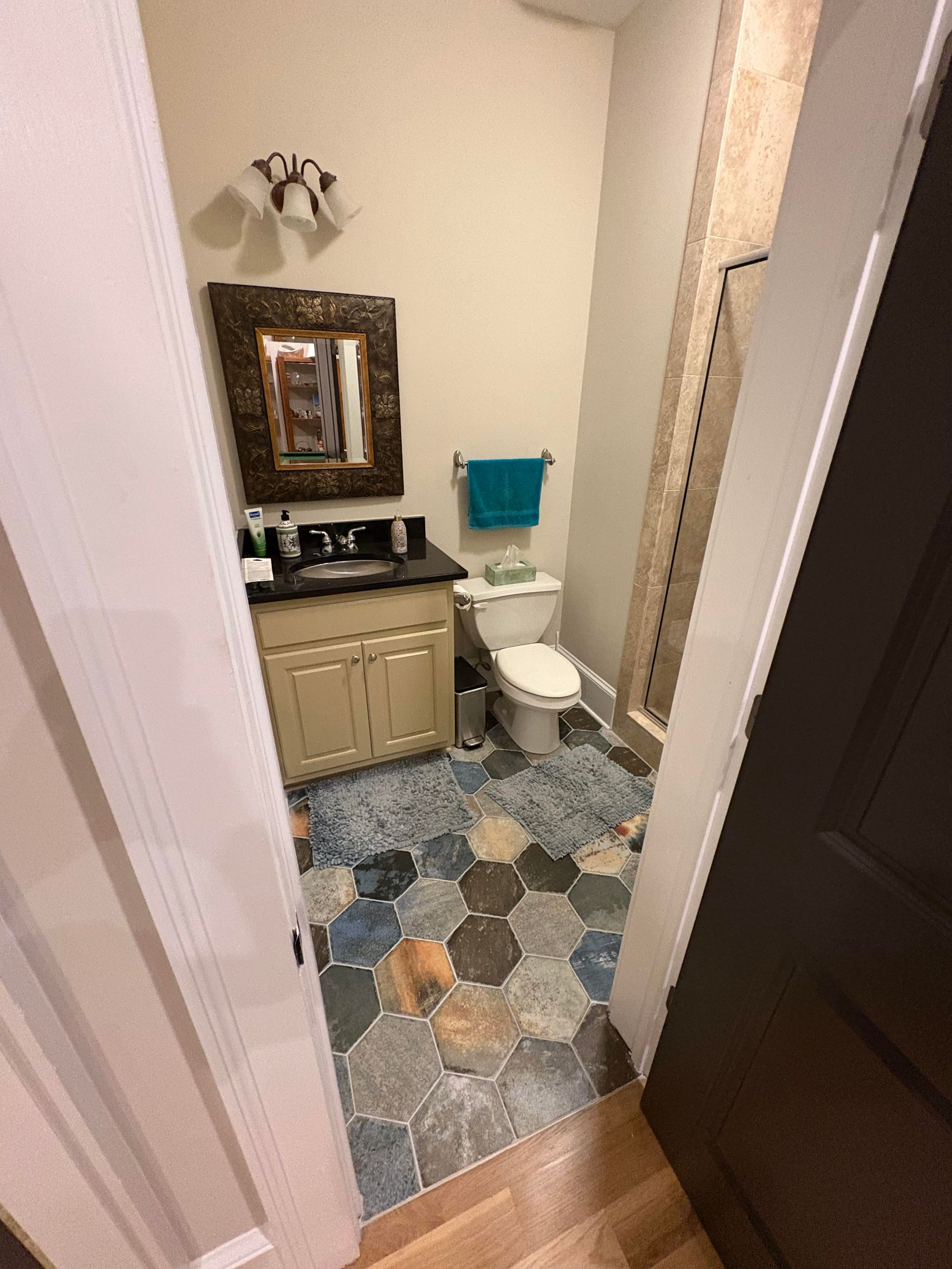 A small bathroom with patterned tile floor, toilet, vanity with mirror, and shower.