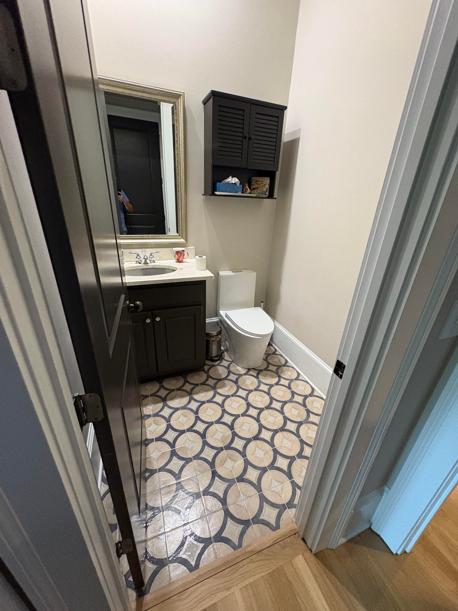 Small bathroom with patterned floor, dark cabinets, and a gold-framed mirror.