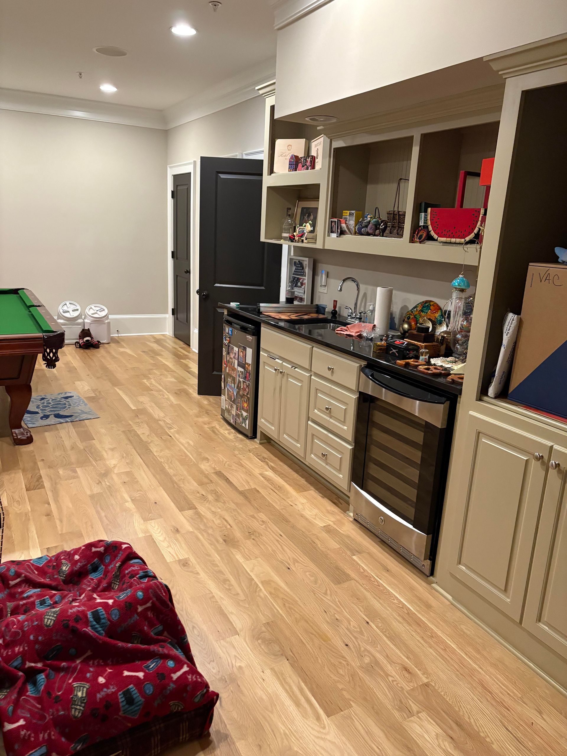 A room with a small kitchen and a pool table. Wooden floors, tan cabinets, and a beanbag chair.