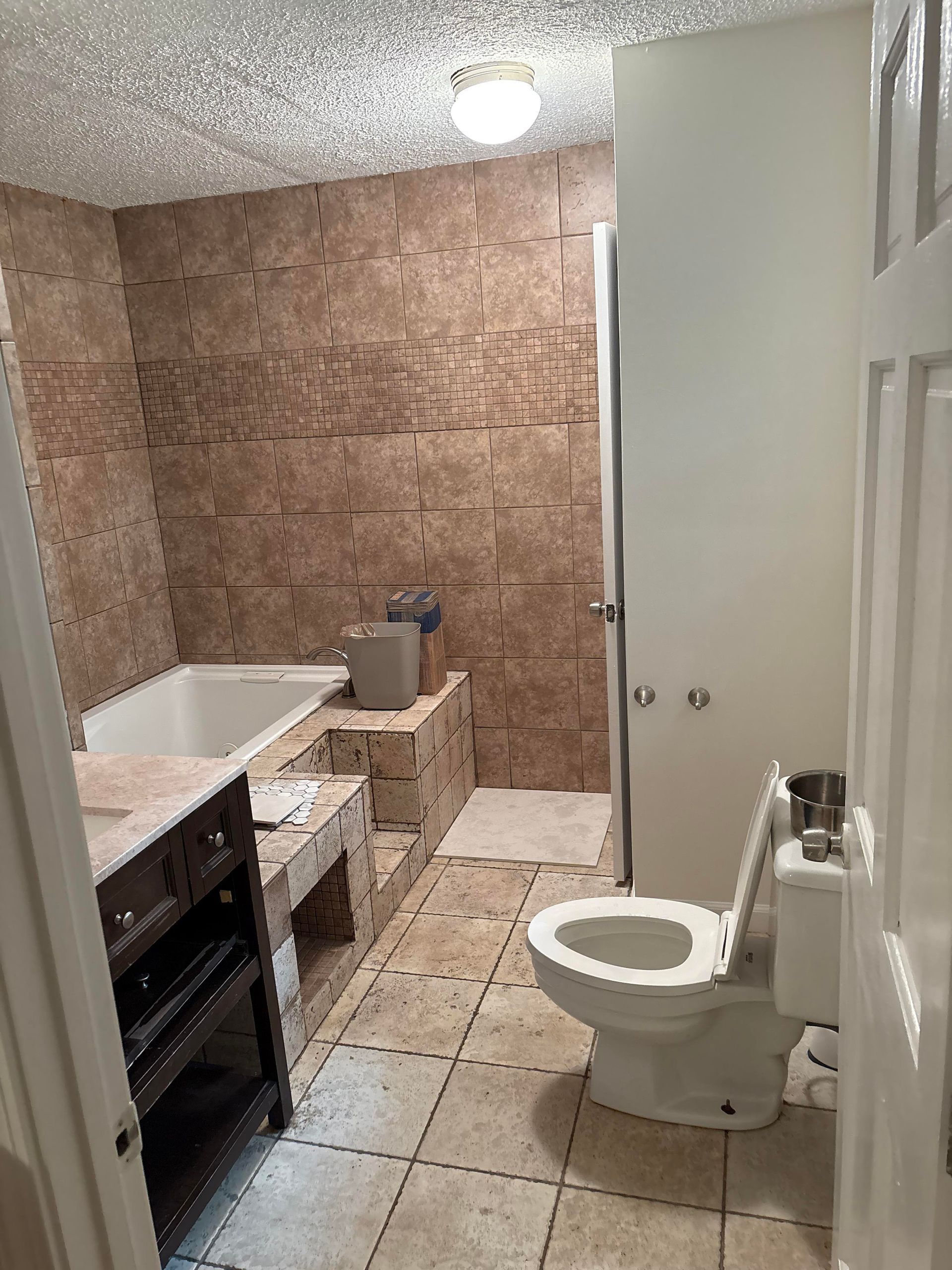Bathroom with beige tiled walls, white toilet, bathtub, and vanity.
