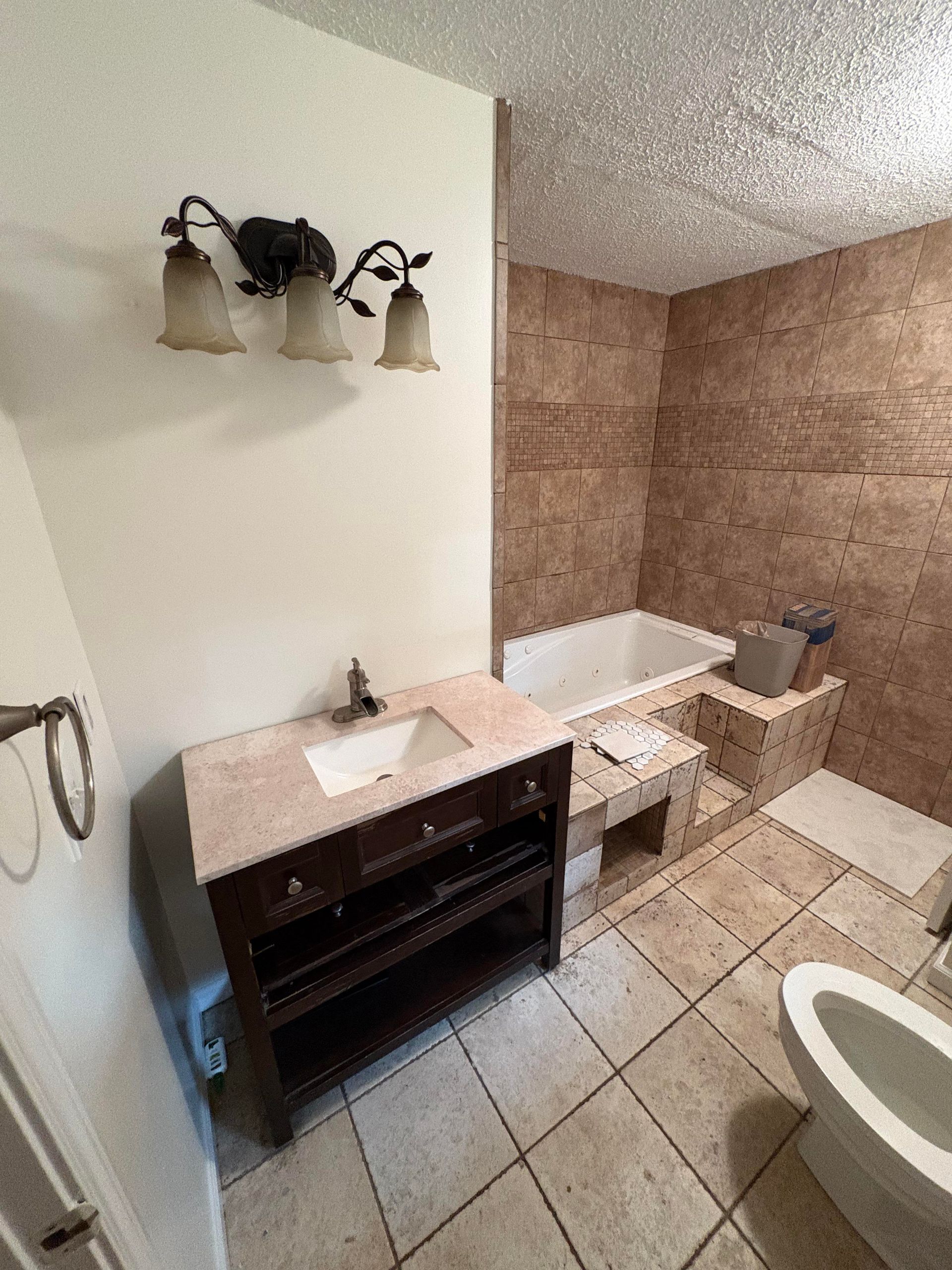 Bathroom with vanity, toilet, and tub; beige walls and tile, dark wood vanity.