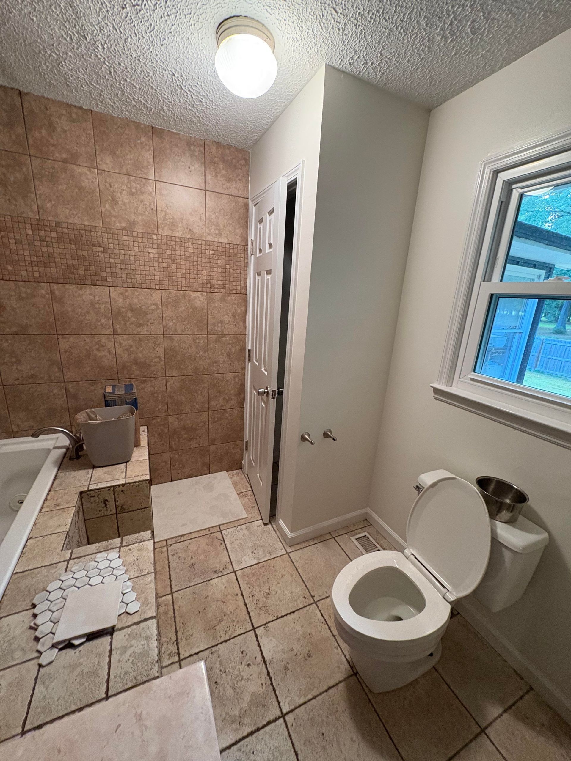 Bathroom with tiled floor and walls, toilet, and a window; one wall has brown textured material.