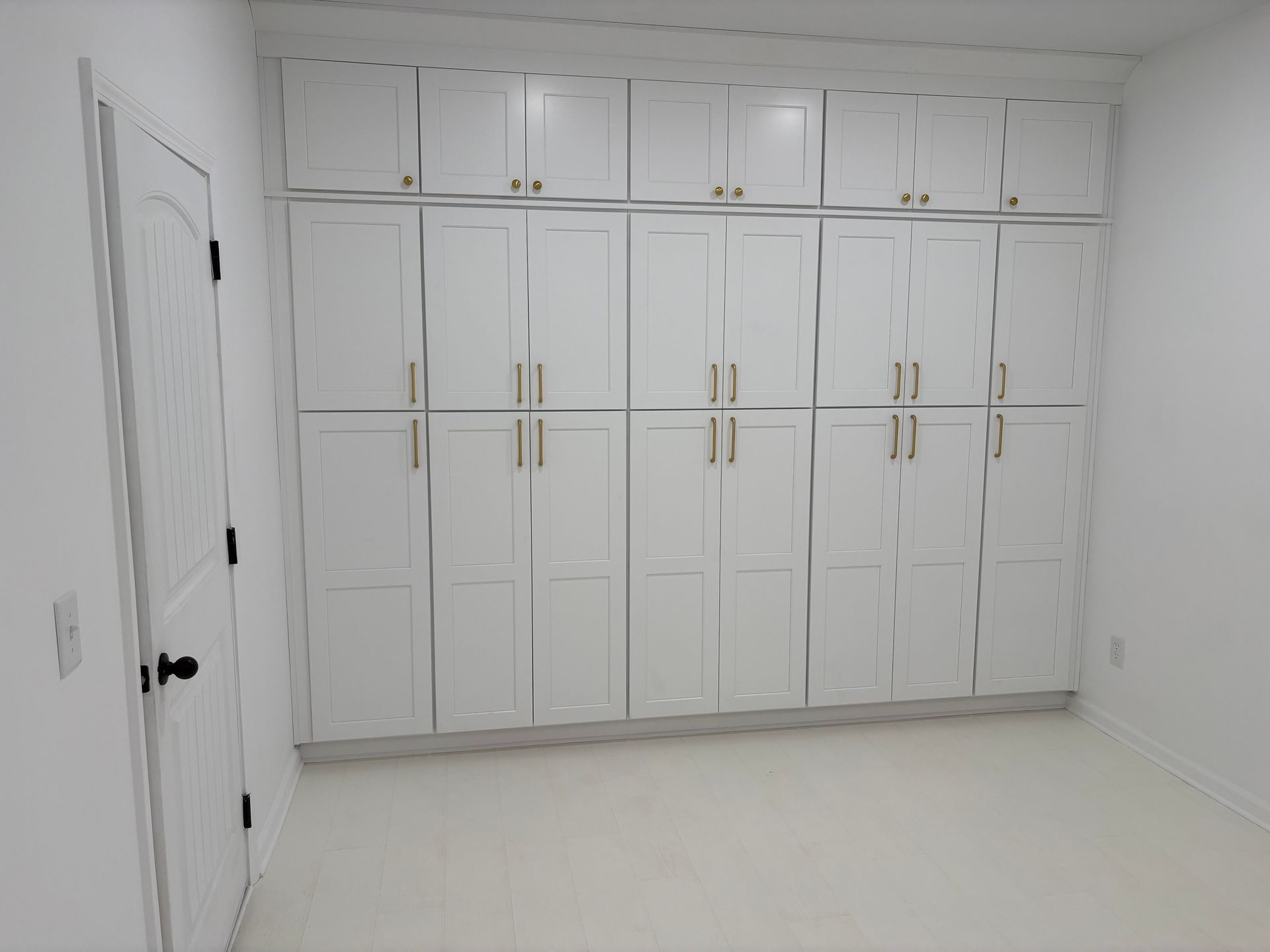 White cabinets on a white wall in a room, with a closed white door on the left side.