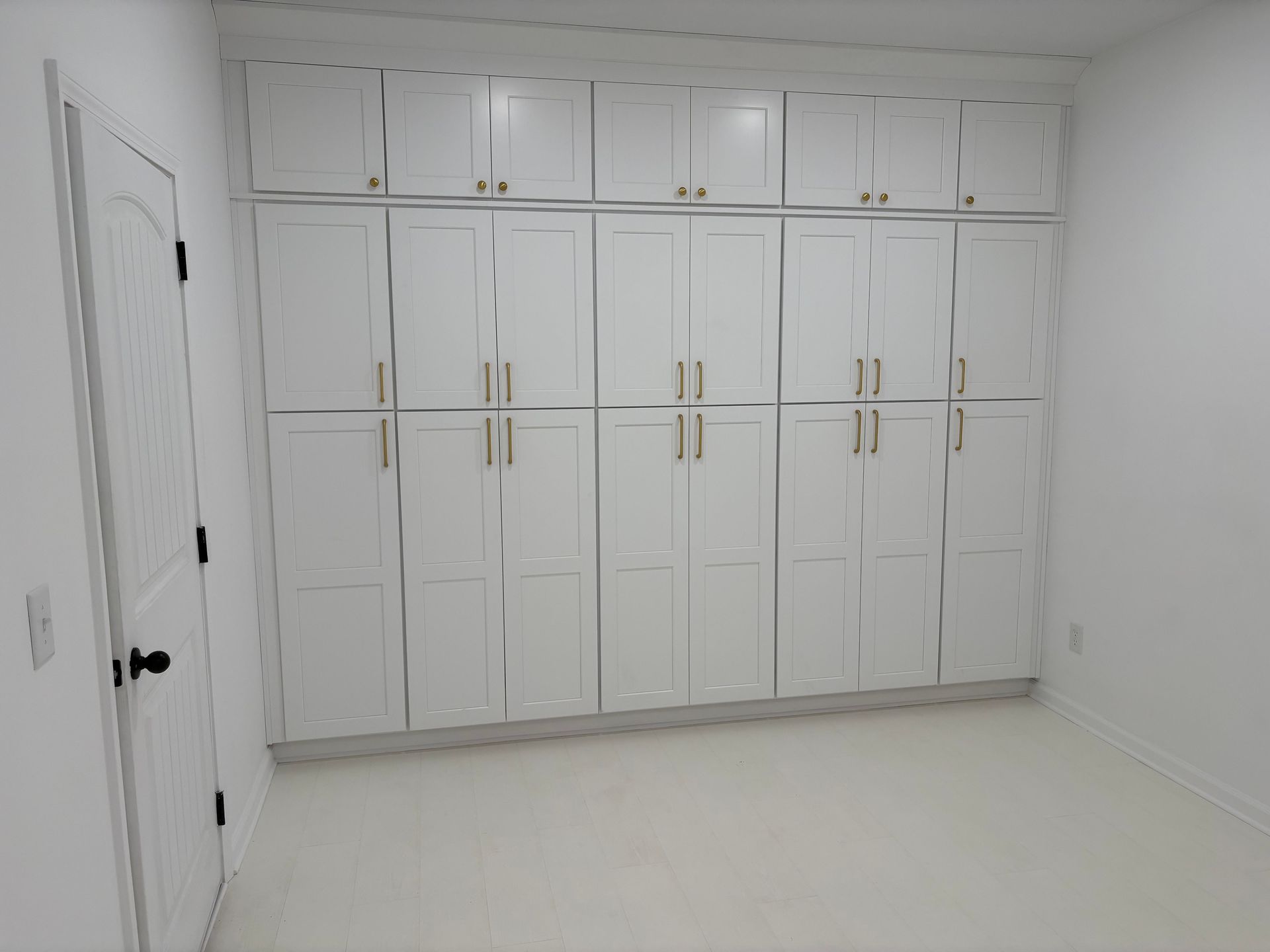 White built-in storage cabinets spanning a wall, with gold hardware and a white door to the left.