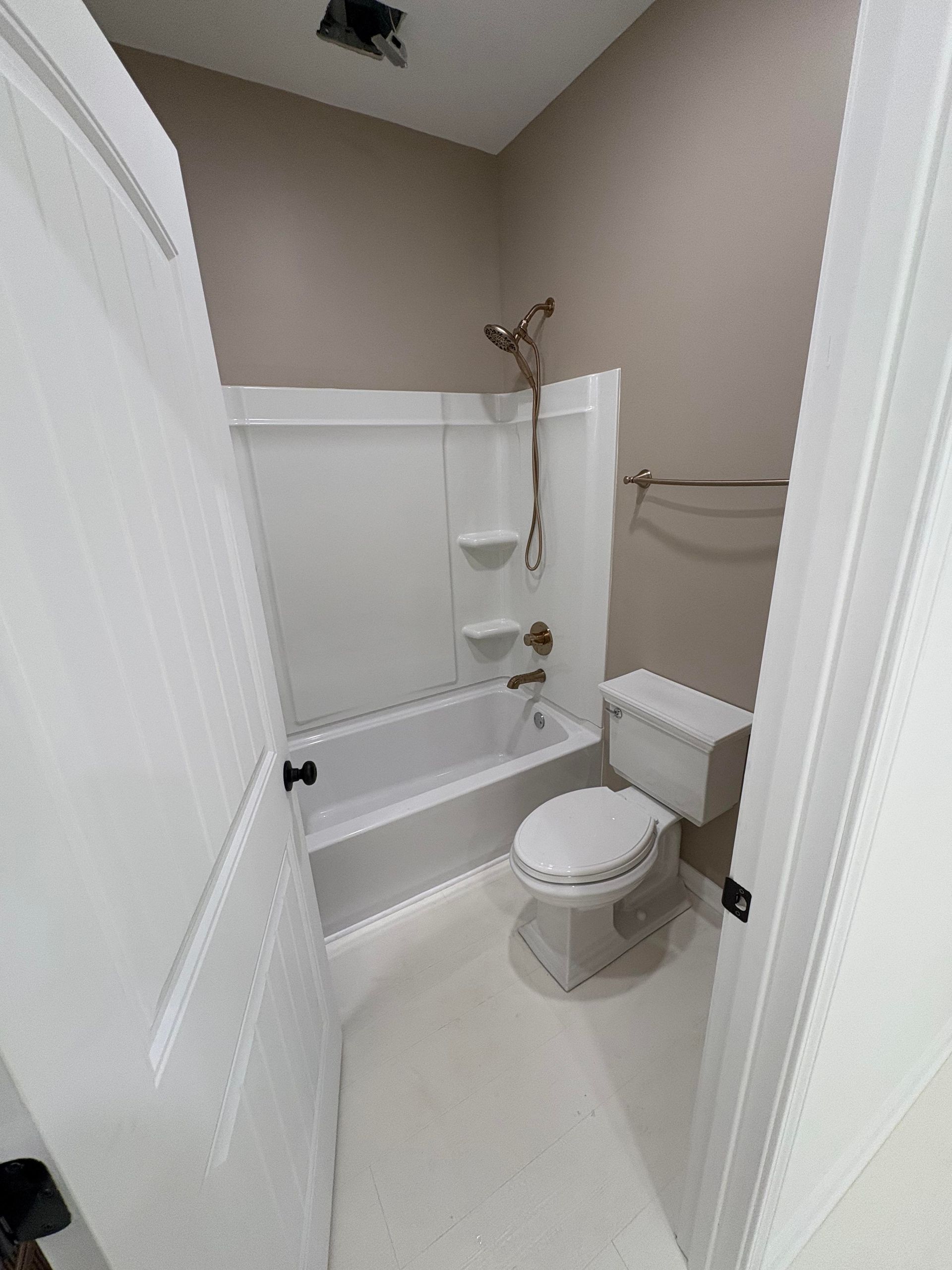 Small bathroom with a white tub and toilet, tan walls, and a towel rack.