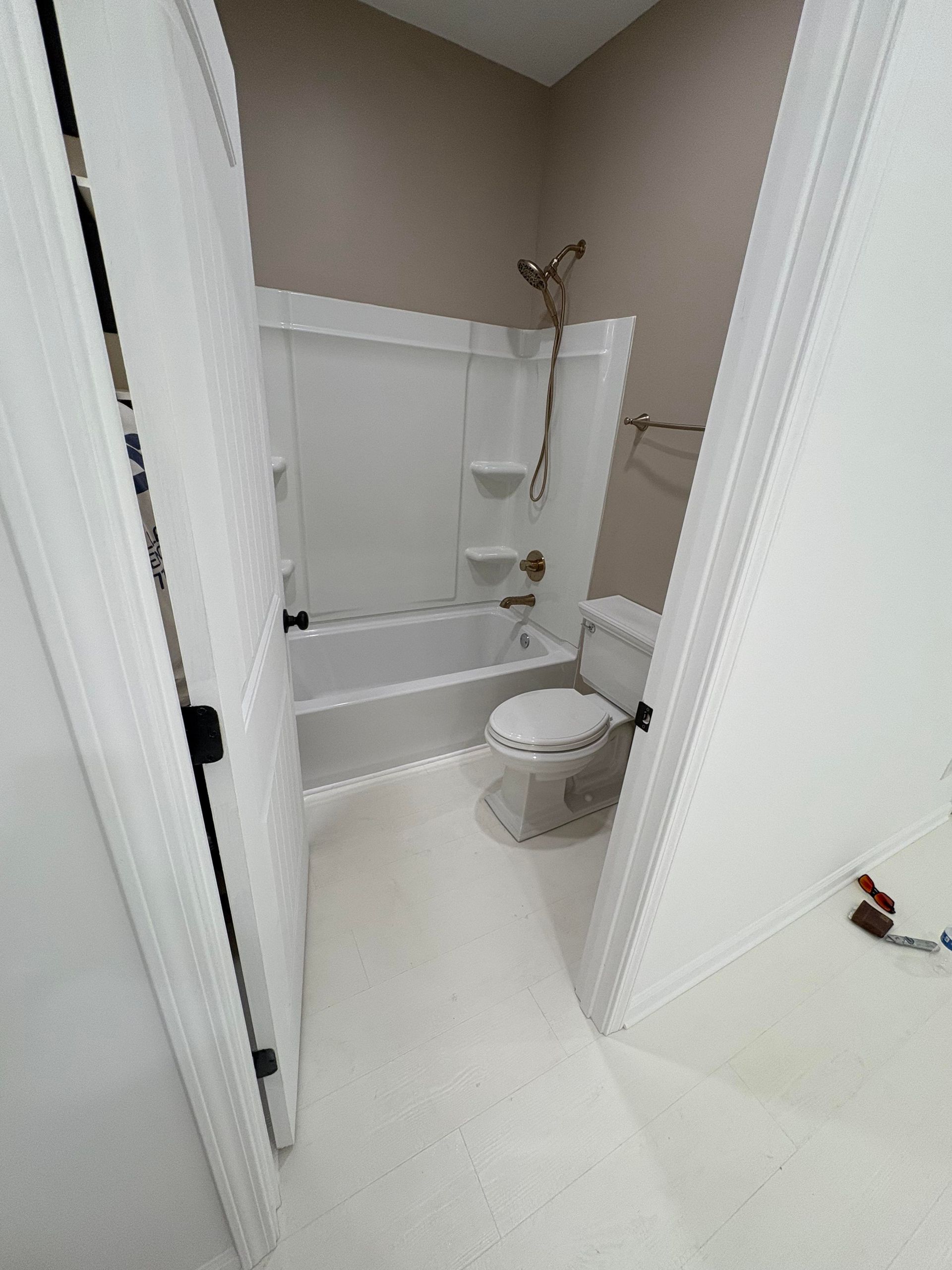 Bathroom with white tub, toilet, and walls; tan upper wall.