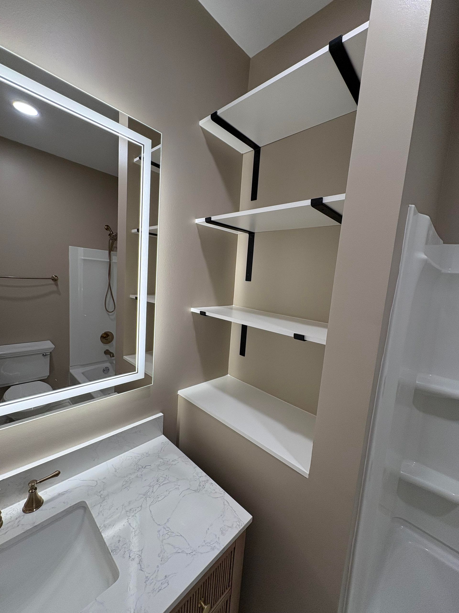 Bathroom with white shelves supported by black brackets, beside a mirror and vanity.