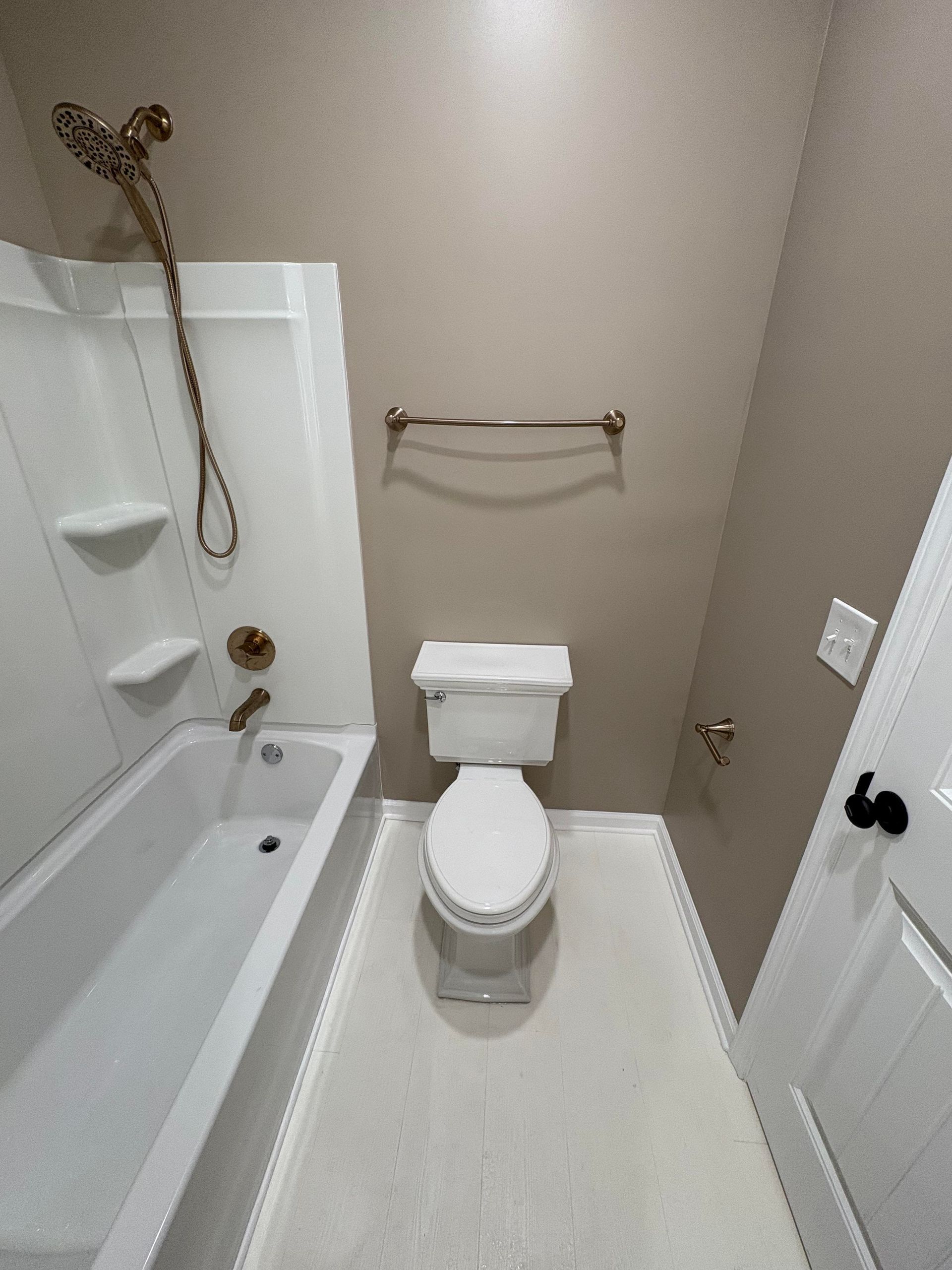 Bathroom with white tub, toilet, and beige walls, with bronze fixtures.