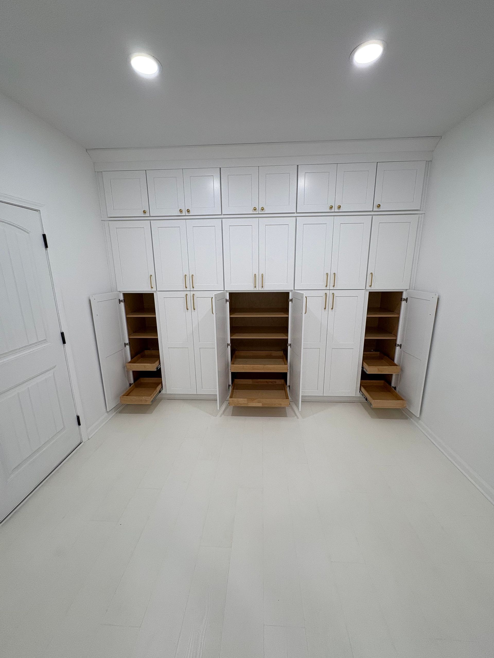 White cabinets line a room's wall, doors open. Shelves are visible inside. The space is bright.