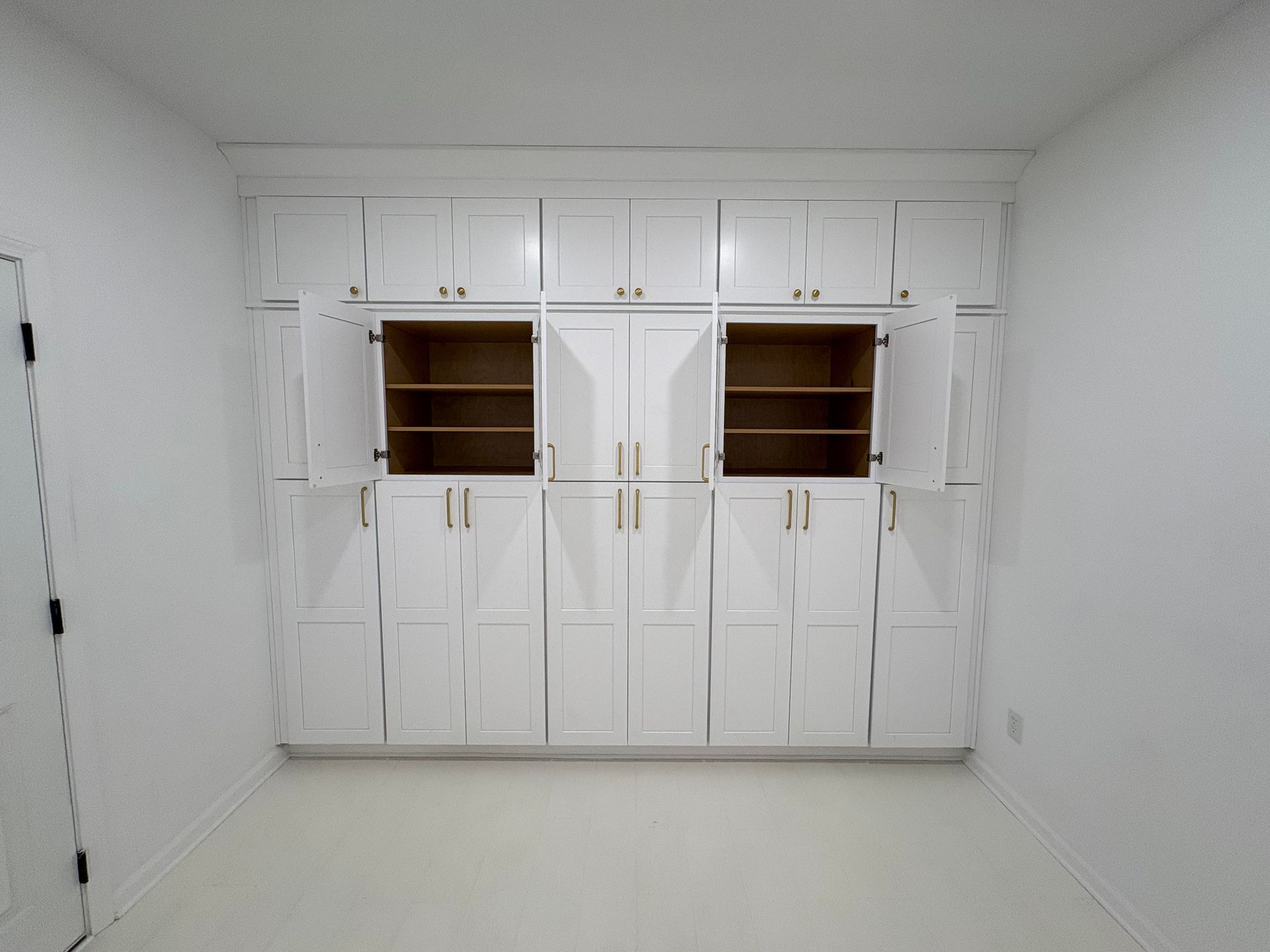 White cabinets fill a wall in a room; some doors are open, revealing shelves.