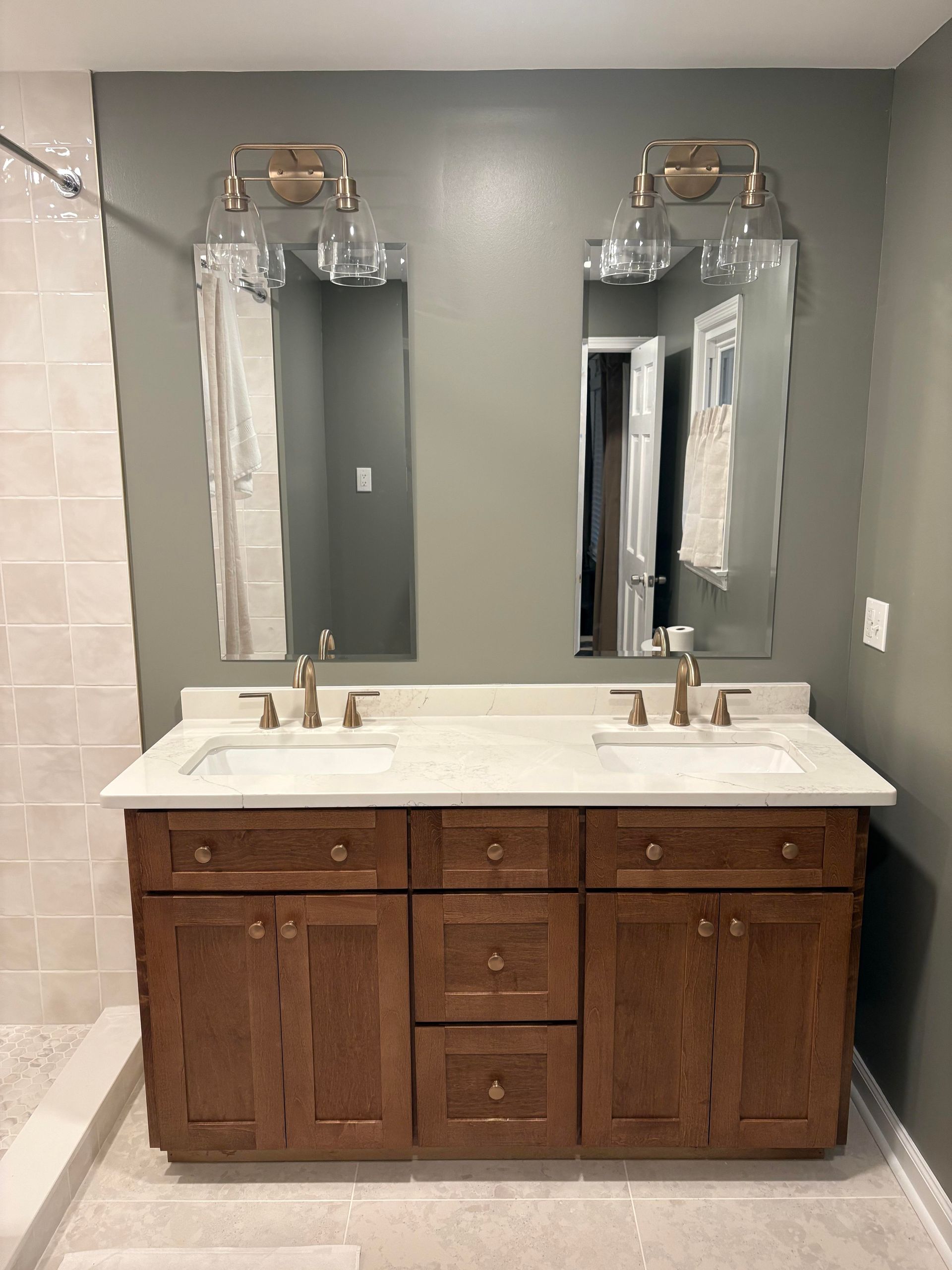 Bathroom with double vanity, two mirrors, brown cabinets, and gray walls.