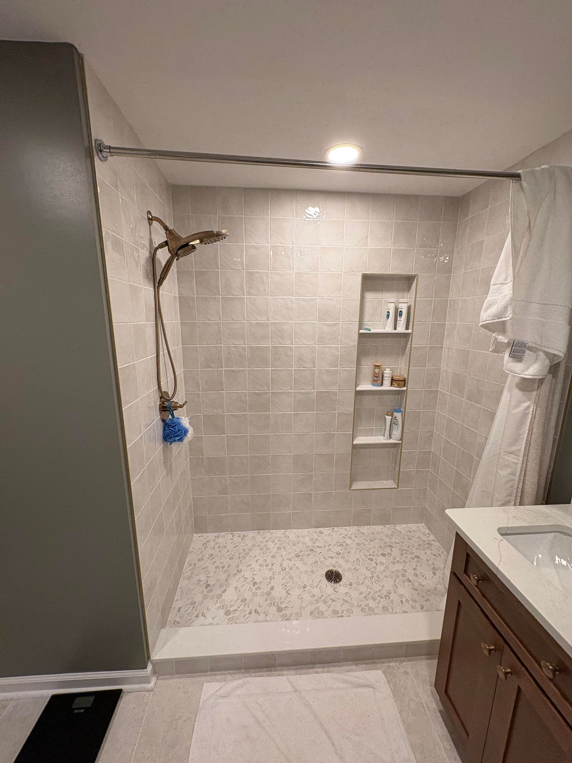Tiled shower with built-in shelves and bronze fixtures. A white robe hangs from a shower curtain rod.