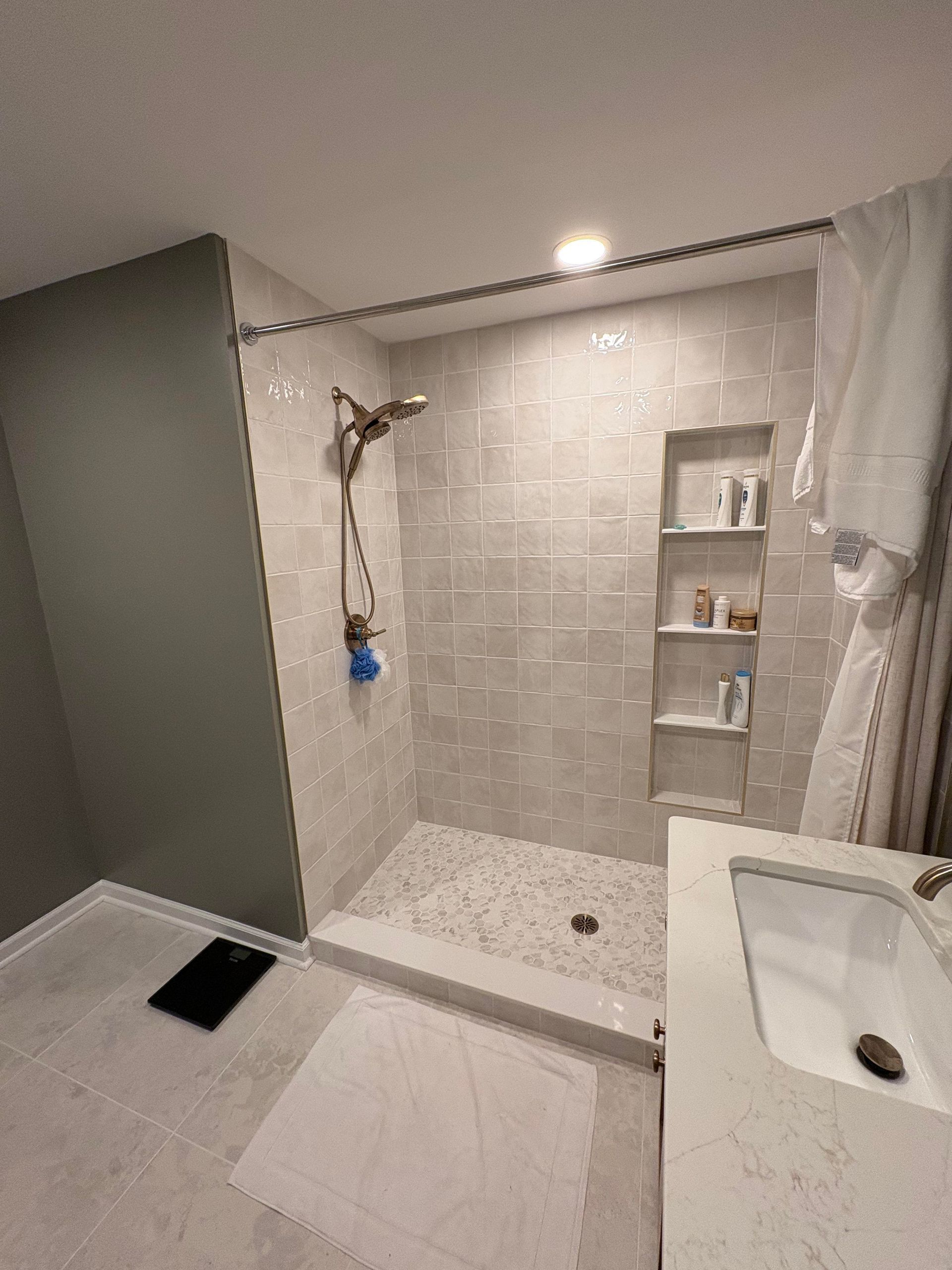 Modern bathroom with a tiled shower, built-in shelving, and a white sink.