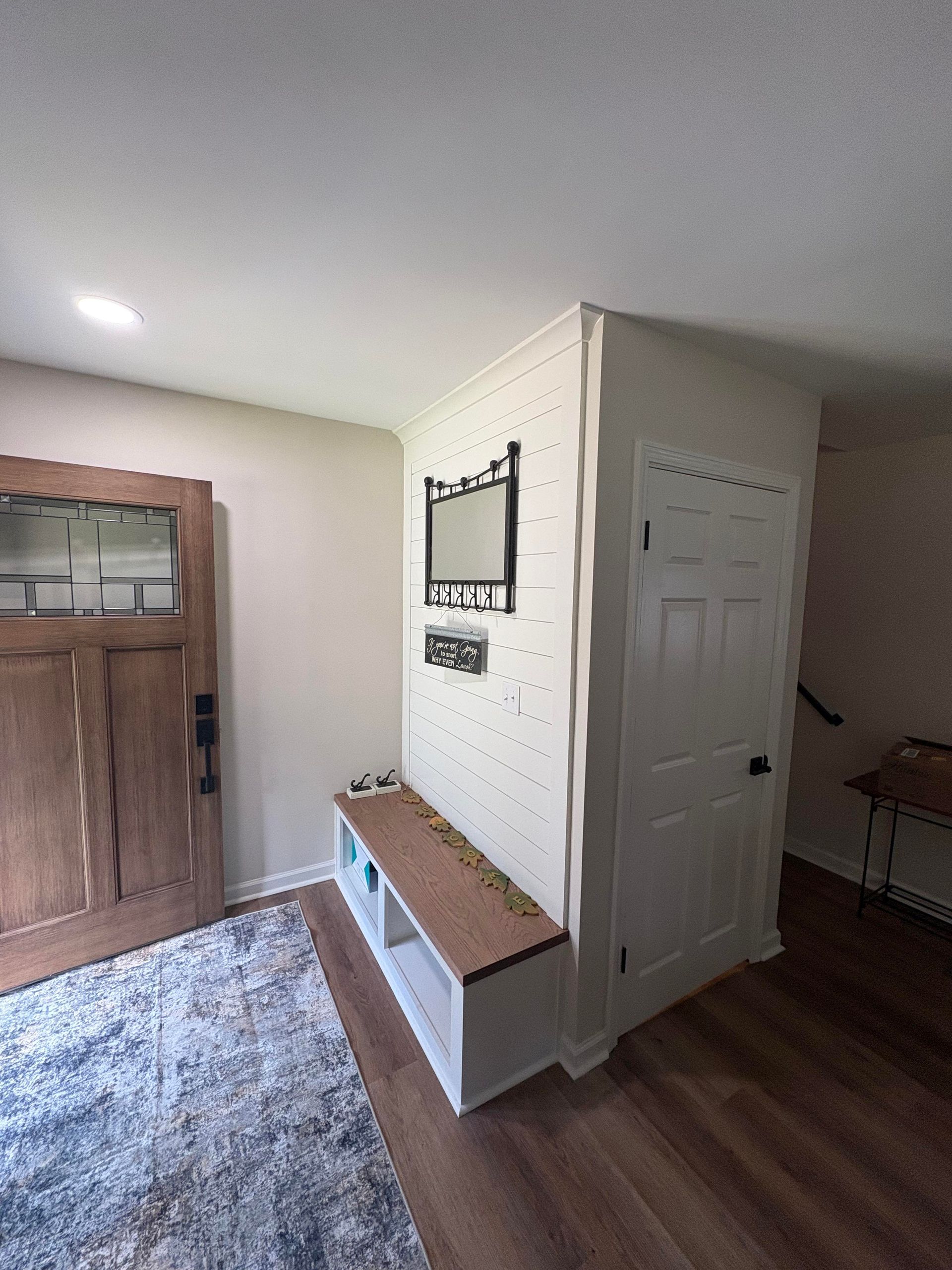 Entryway with wooden door, bench, and decorative mirror and shelf on white wall.