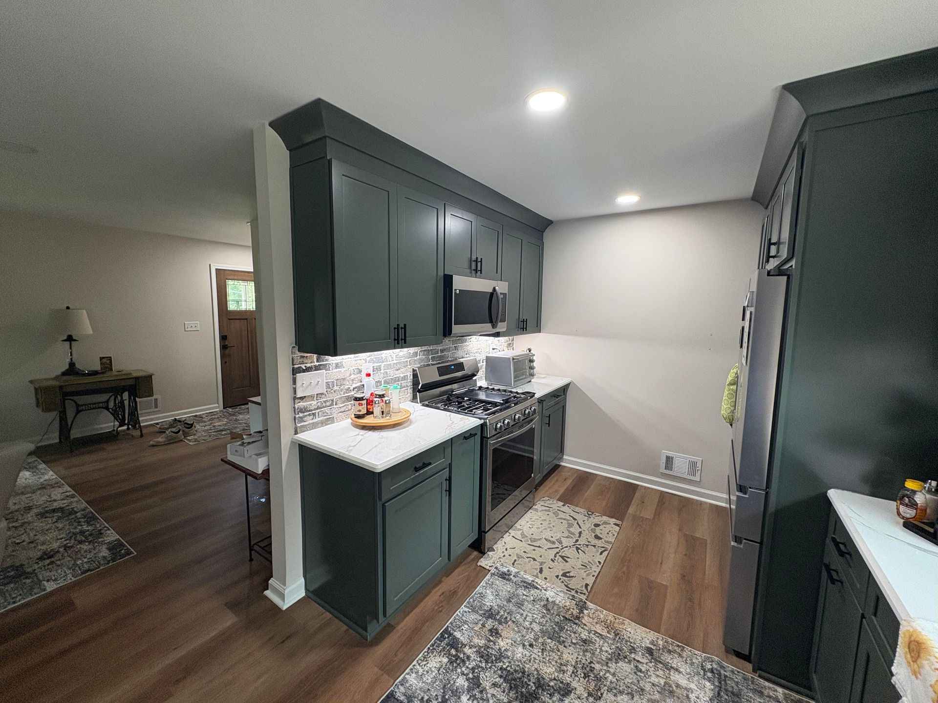 Green kitchen cabinets with white countertops, stainless steel appliances, and wood flooring.