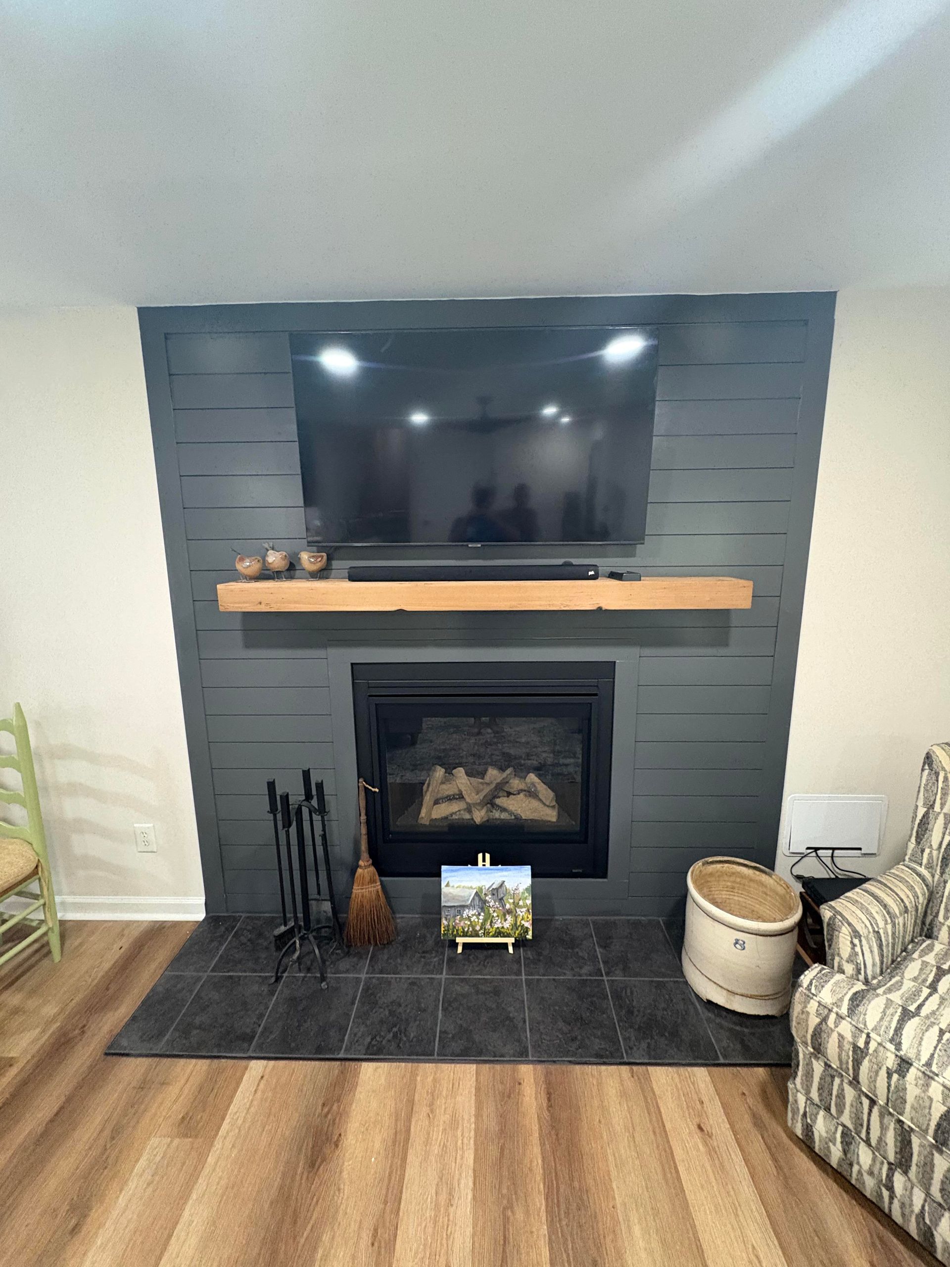 Fireplace with dark gray paneled wall, mounted TV, wooden mantel, and black hearth.