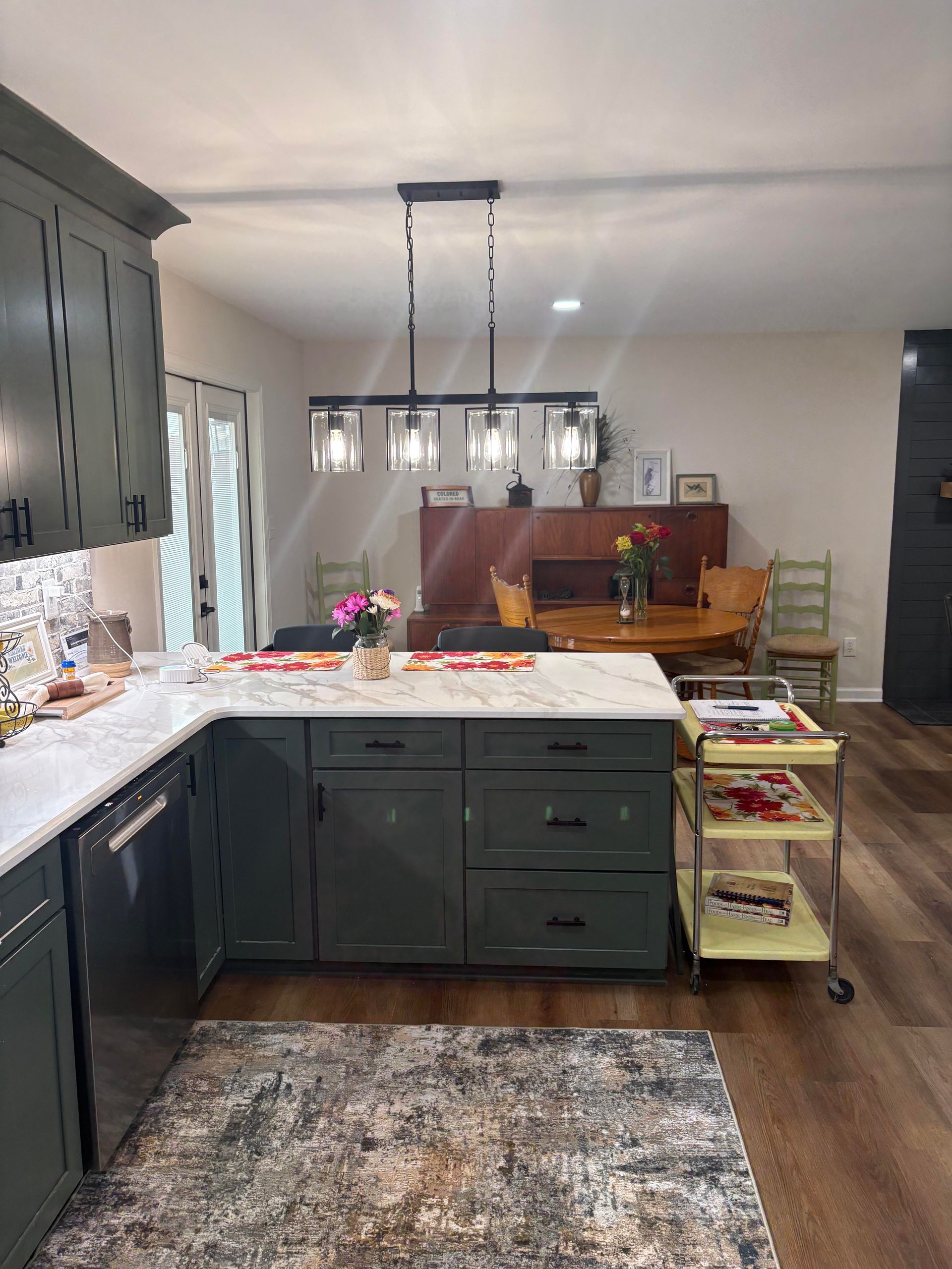 Green kitchen with white countertops and island, dark wood floors, dining area in background.