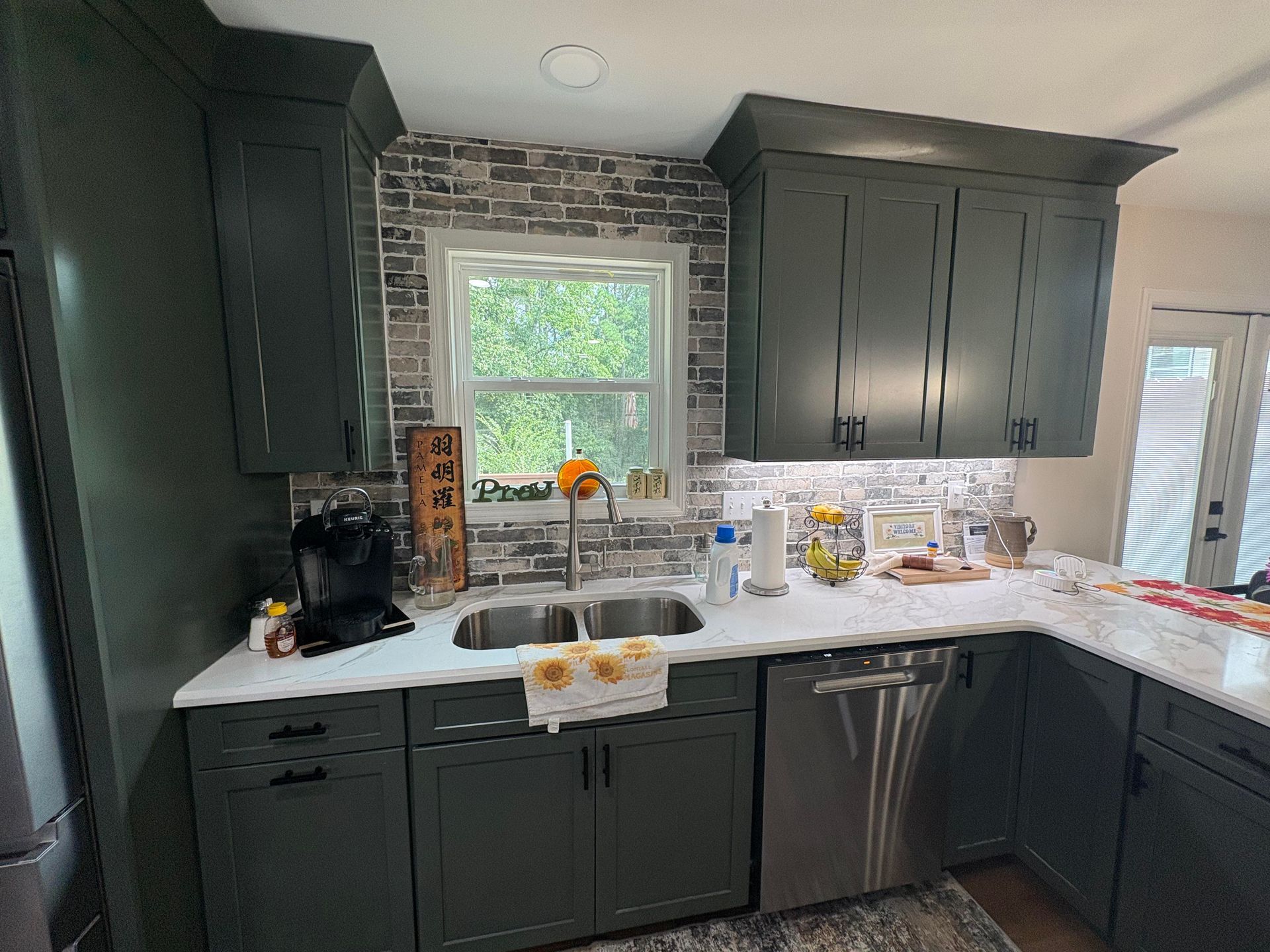 Green kitchen cabinets with a brick backsplash, white countertops, and stainless steel appliances.