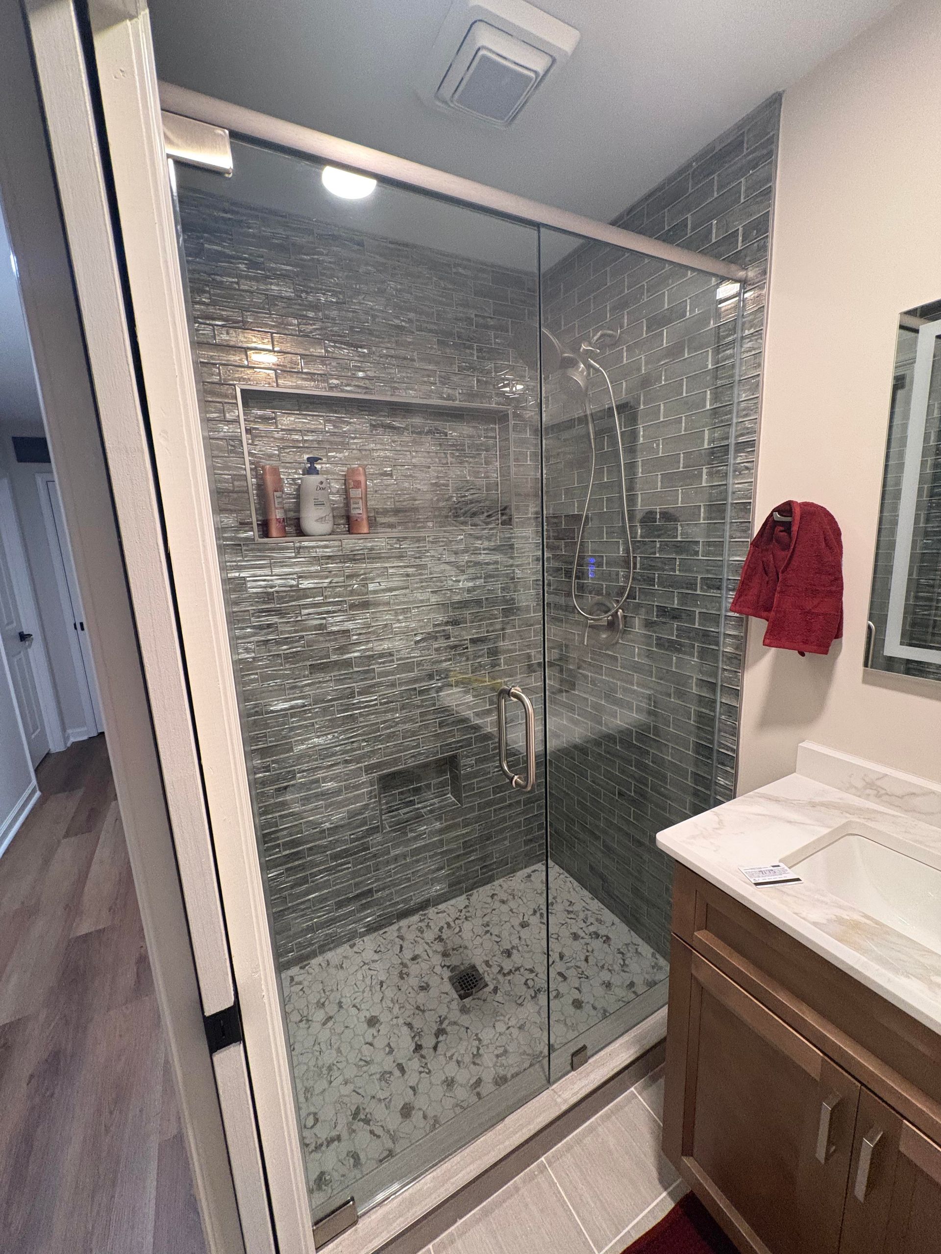 Glass shower with mosaic tile walls, built-in shelf, and a wood vanity in a bathroom.