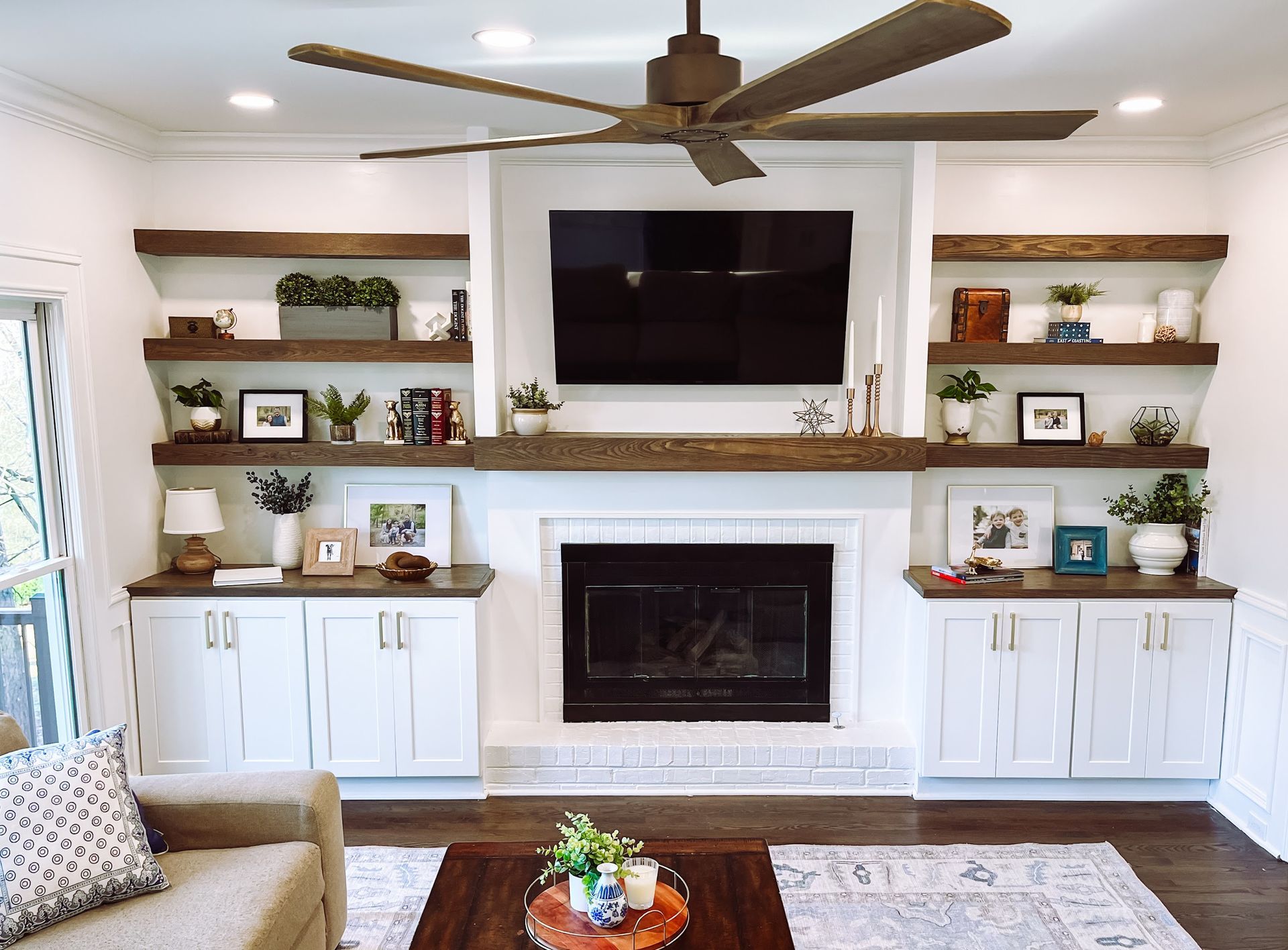 Living room with white built-ins flanking a fireplace. The mantel holds a TV, and open shelving displays decor.