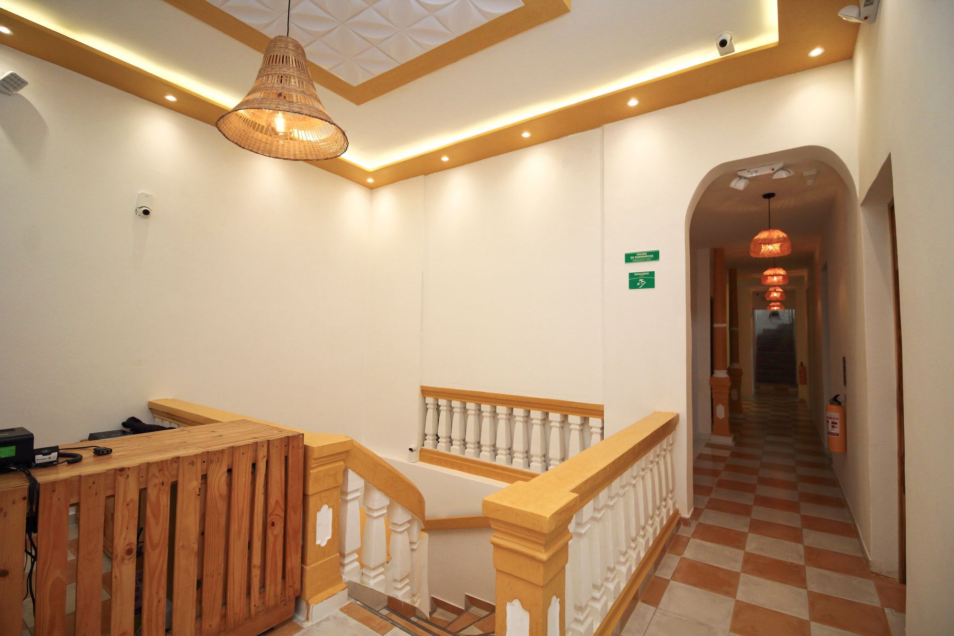 Pasillo interior con mostrador de recepción de madera, escalera y puertas arqueadas que dan a un suelo ajedrezado.