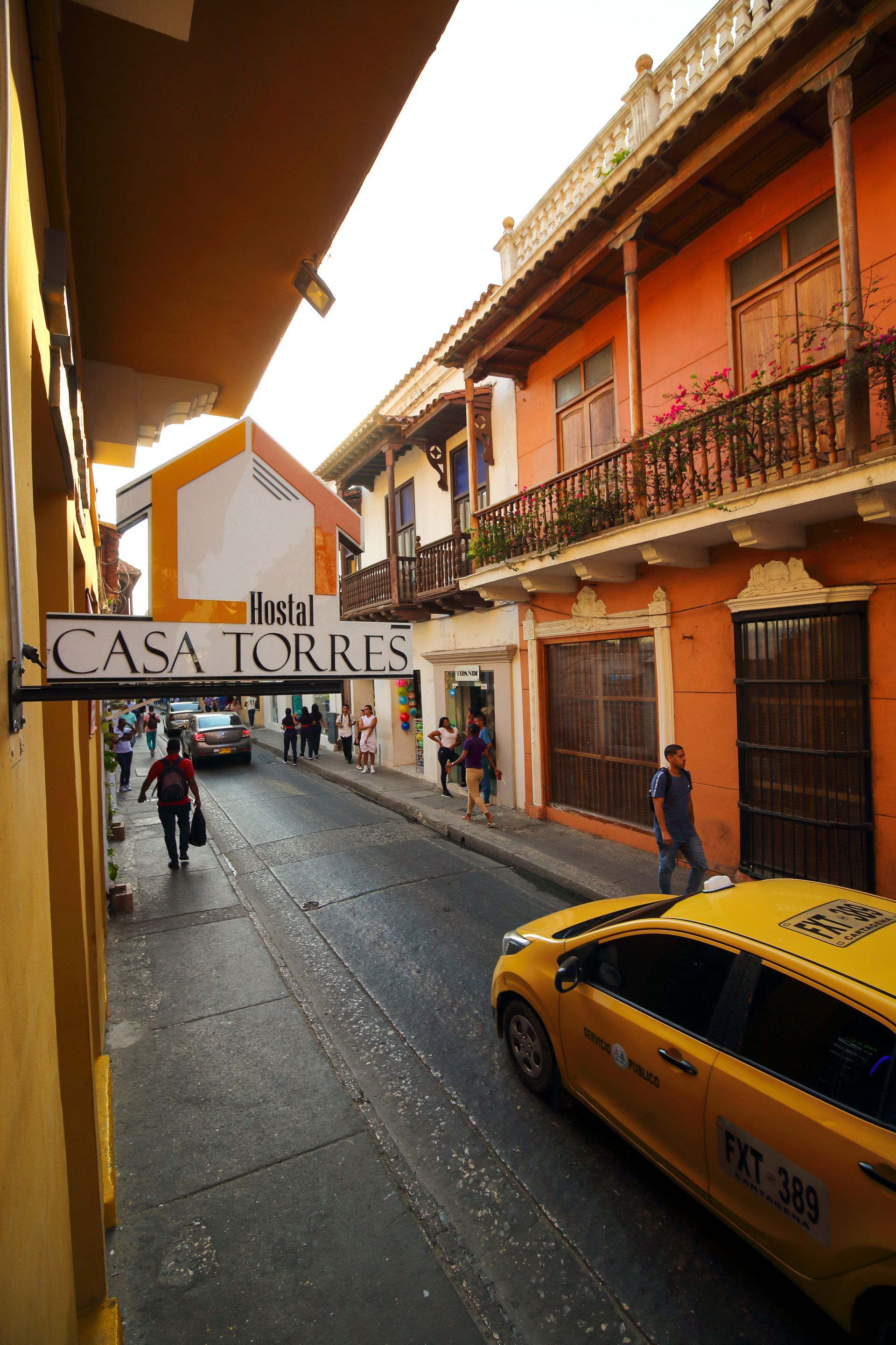 Calle estrecha en Cartagena, Colombia, con edificios coloridos, un taxi y peatones. Letrero del Hotel Casa Torres.