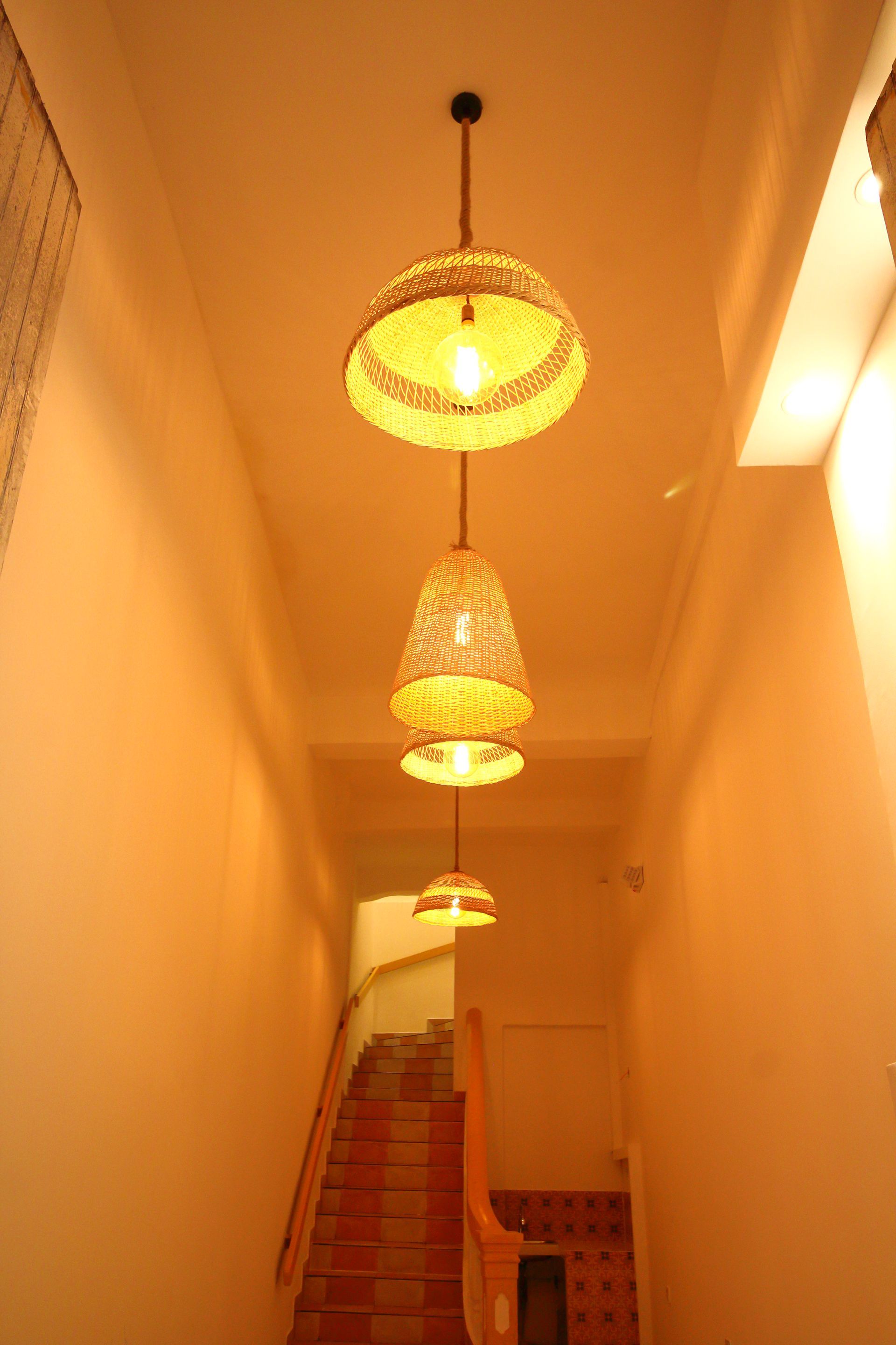 Cuatro lámparas colgantes de mimbre penden sobre una escalera con escalones de ladrillo y paredes blancas.