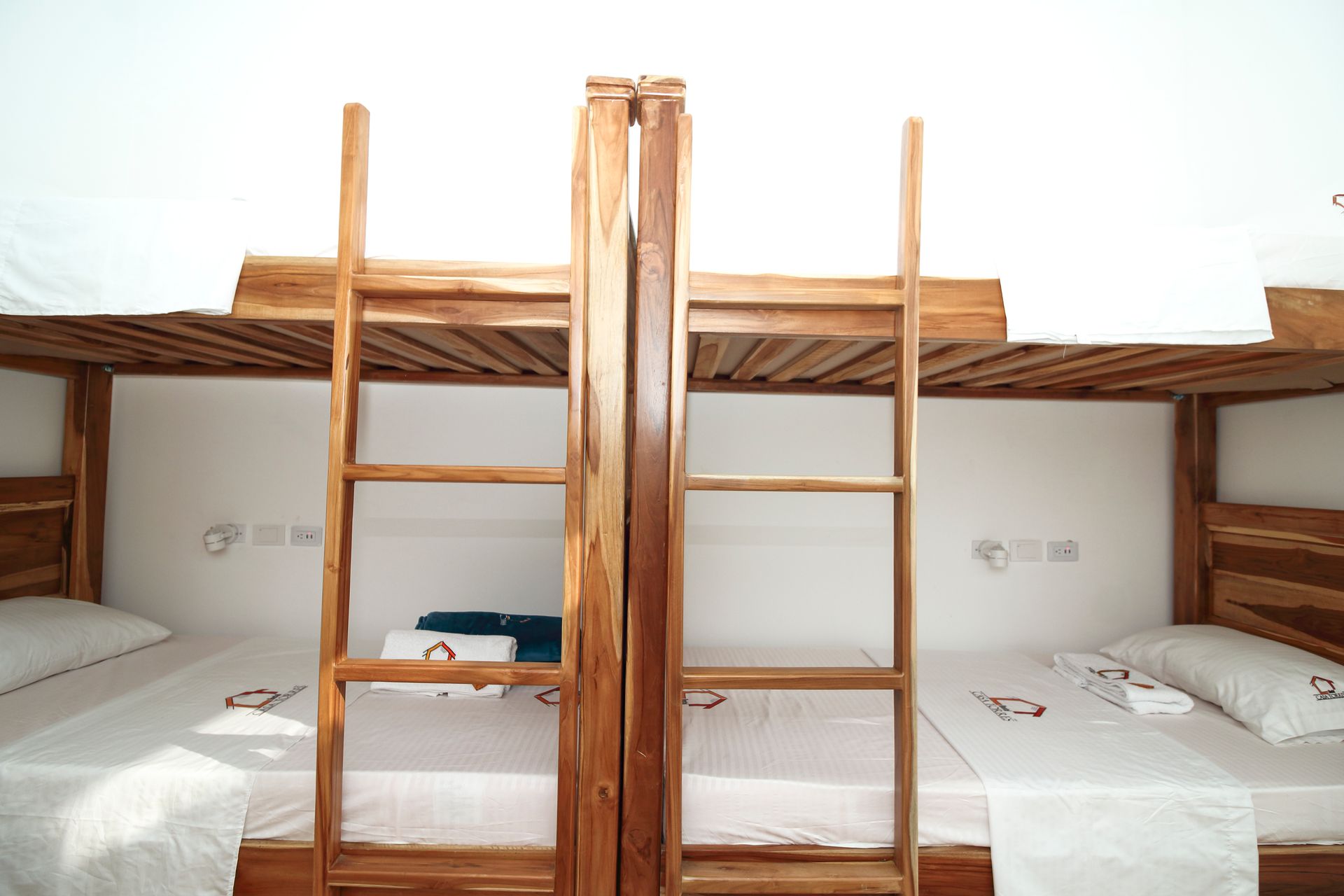 Literas de madera en una habitación blanca, con escaleras, ropa de cama blanca y una toalla.