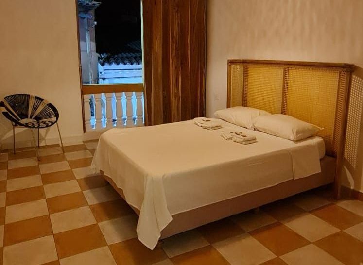 Dormitorio con cama doble, cabecero tejido, balcón y suelo estampado.